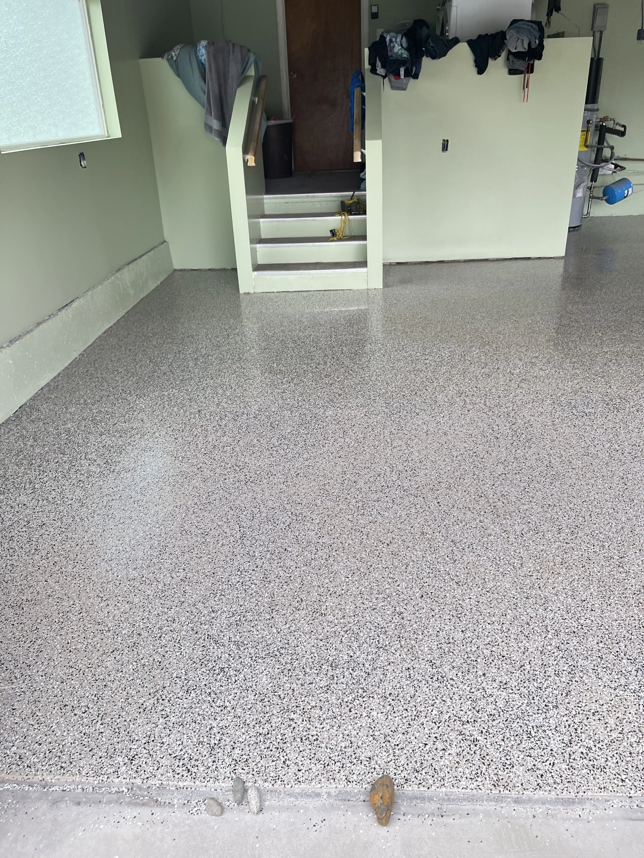 Garage with freshly epoxy-coated floor, stairs leading to a door, and laundry hanging on hooks.
