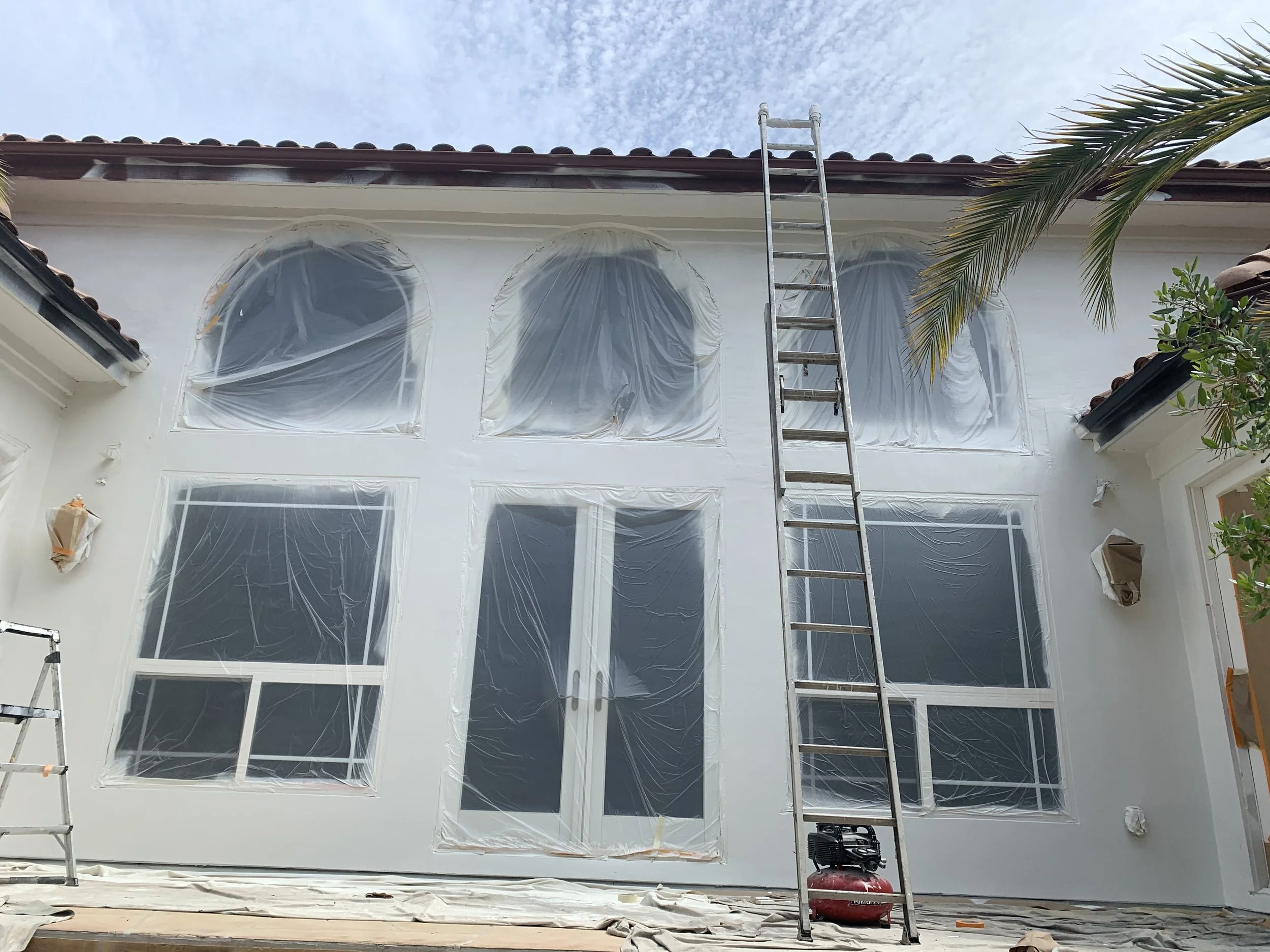 House exterior interior renovation in progress with plastic-covered windows, a ladder, and construction equipment.
