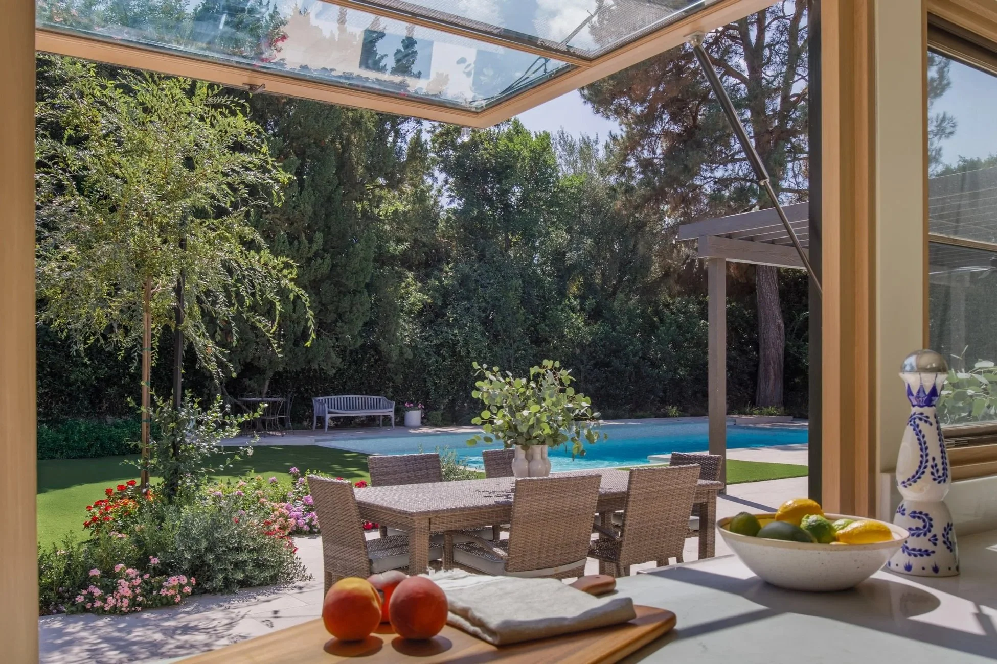 Modern backyard patio with a swimming pool, hot tub, outdoor seating, and a view of hillside houses and greenery.