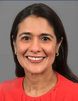 A smiling woman with dark hair, wearing a red top and gold earrings, against a neutral background.