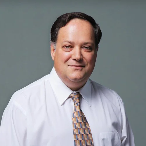 Portrait of a man in a white dress shirt and patterned tie against a gray background.