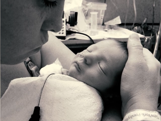 A person holding a sleeping newborn baby wrapped in a blanket.