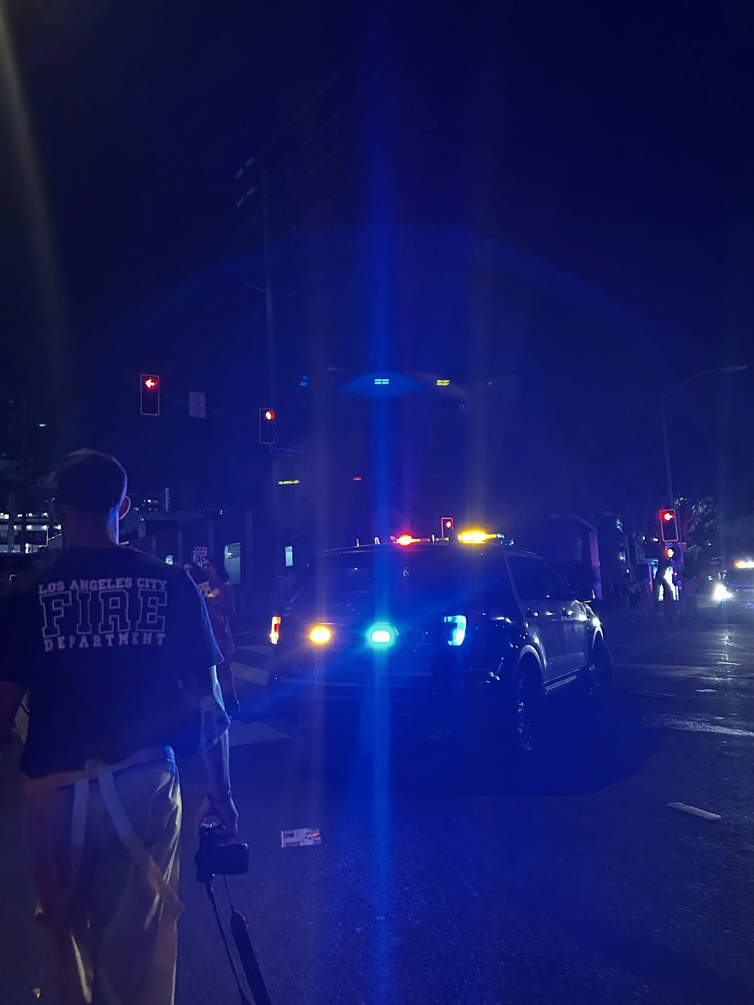 Night scene with emergency vehicles flashing blue and yellow lights as a firefighter walks through the street, capturing the dramatic, cinematic atmosphere of Shy Rockstar Studios.