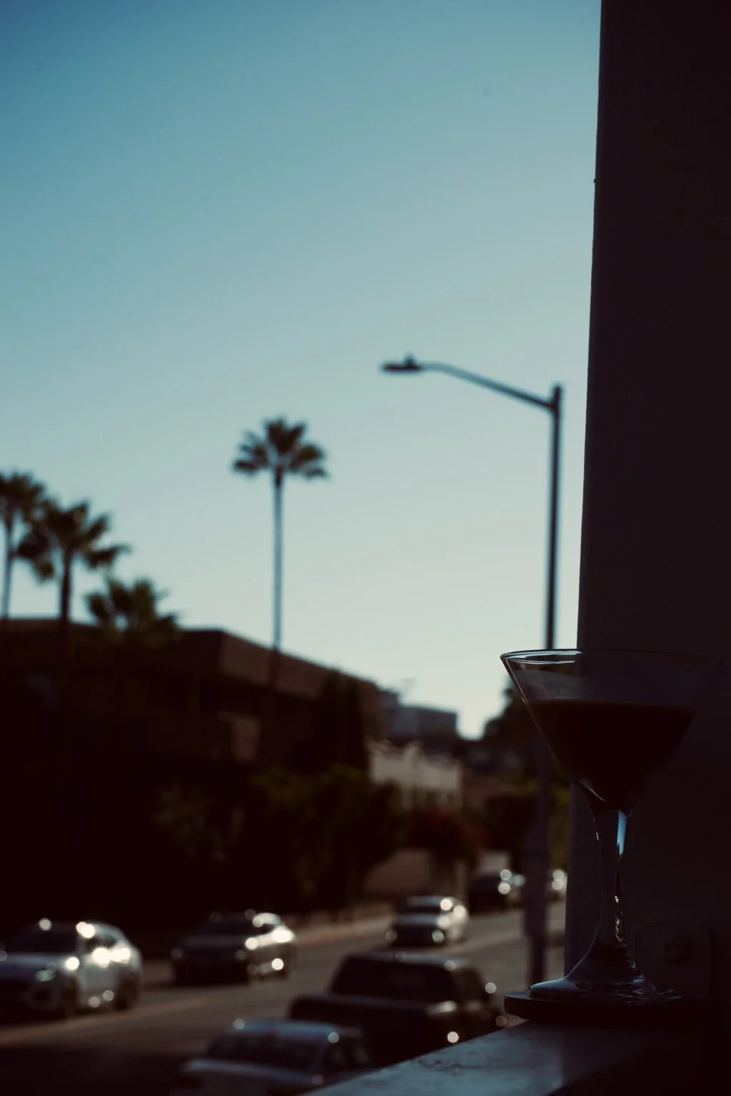 A martini glass silhouetted in the corner of the frame, with palm trees and soft morning light in the background.