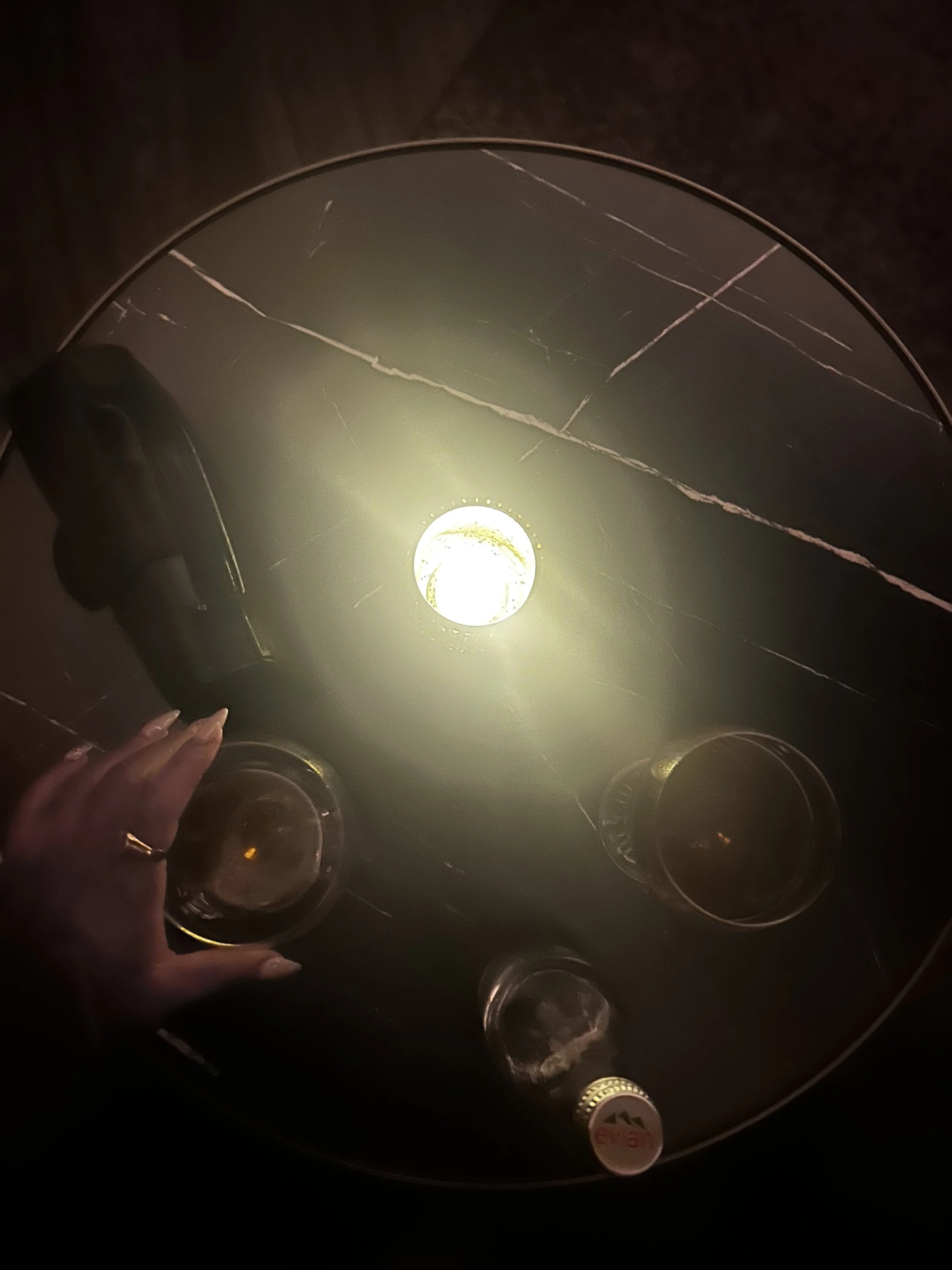 Candlelit table with cocktails and hands resting on marble, captured in low light during a nighttime networking event.