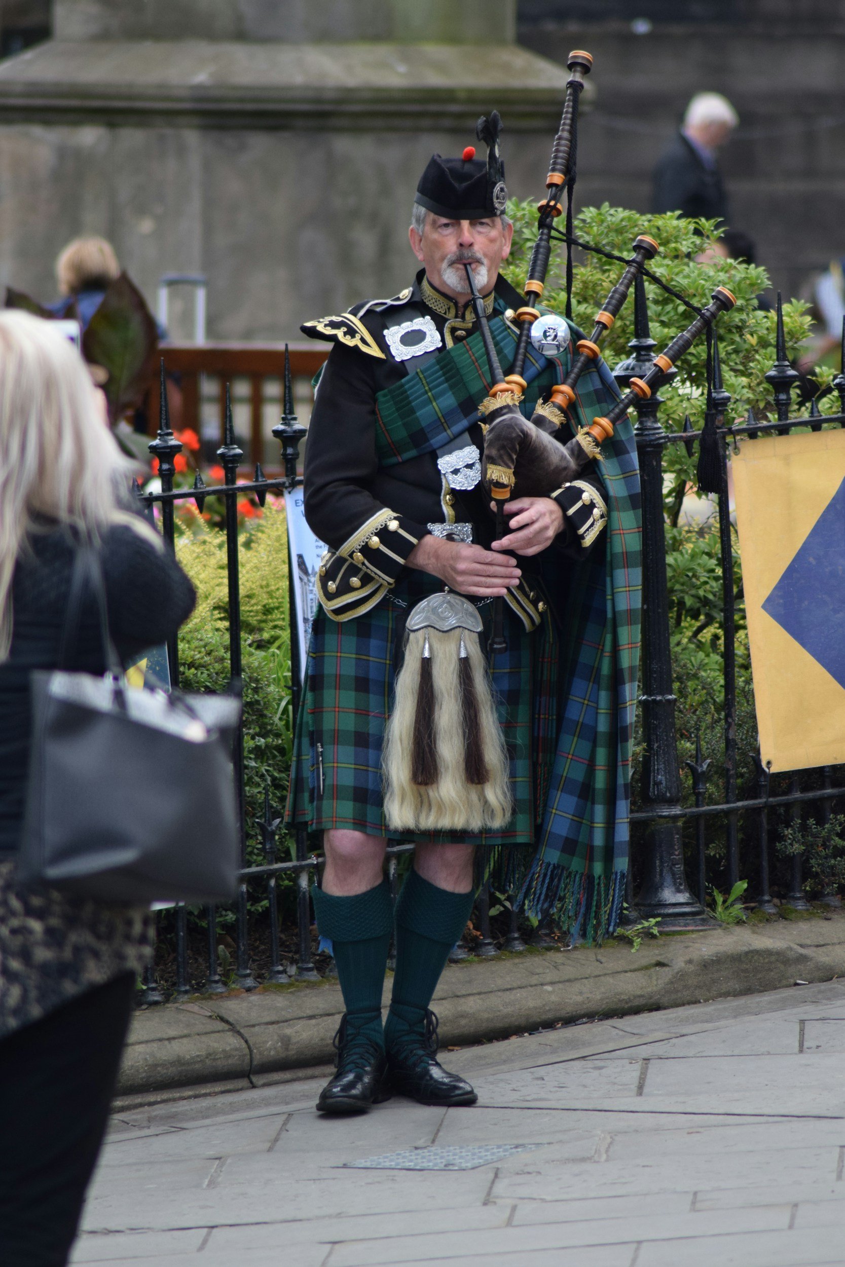 A man dressed in traditional Scottish attire playing bagpipes on the street during a public event.