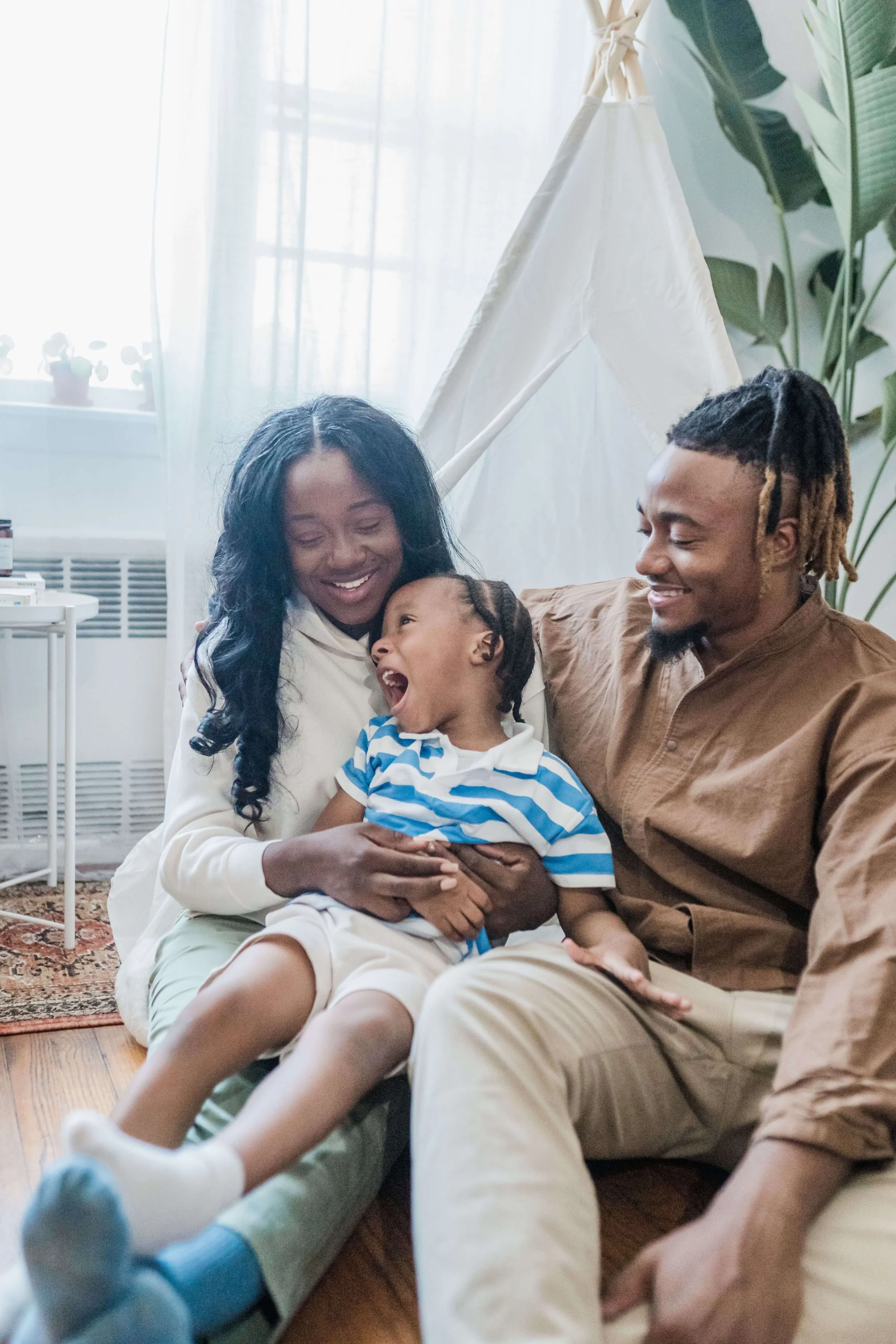 Two parents smiling and laughing with a young child on a couch in a bright living room. Parenting therapy in Los Angeles, CA helps families move from surviving the hard moments to genuinely enjoying the good ones.