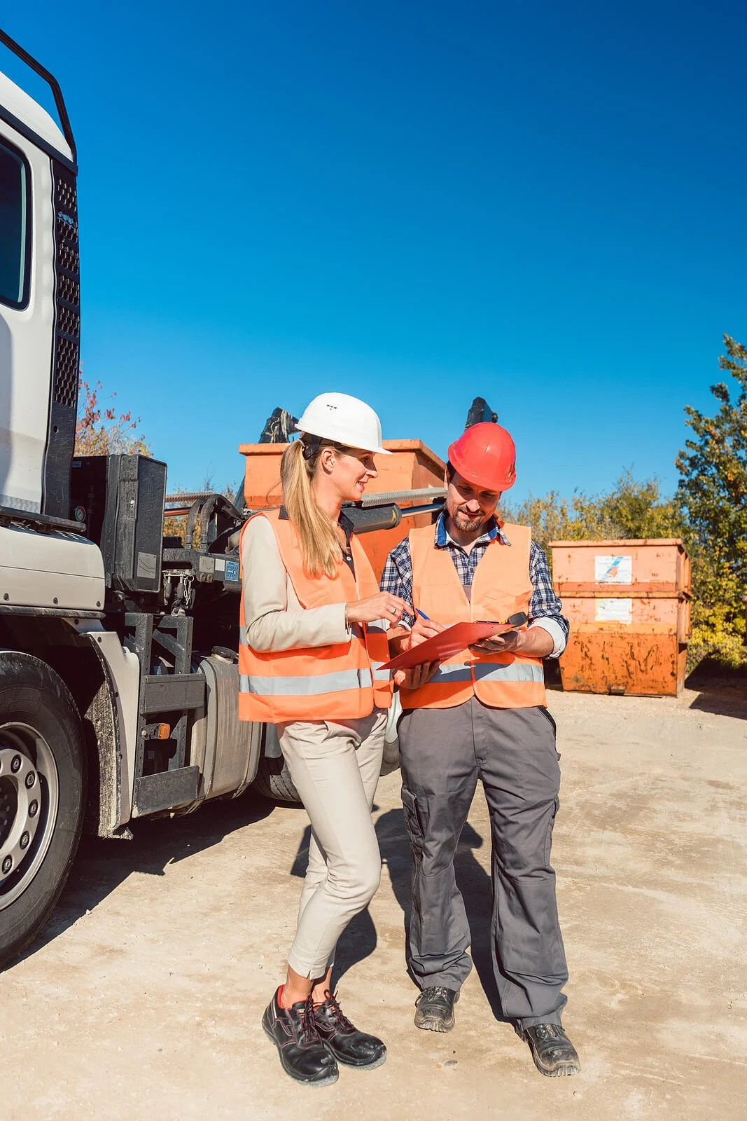 Two safety workers in hard hats and orange vests reviewing a clipboard near commercial truck at outdoor work site. Learn how role separation speeds your return-to-duty with a substance abuse professional in Las Vegas, NV.