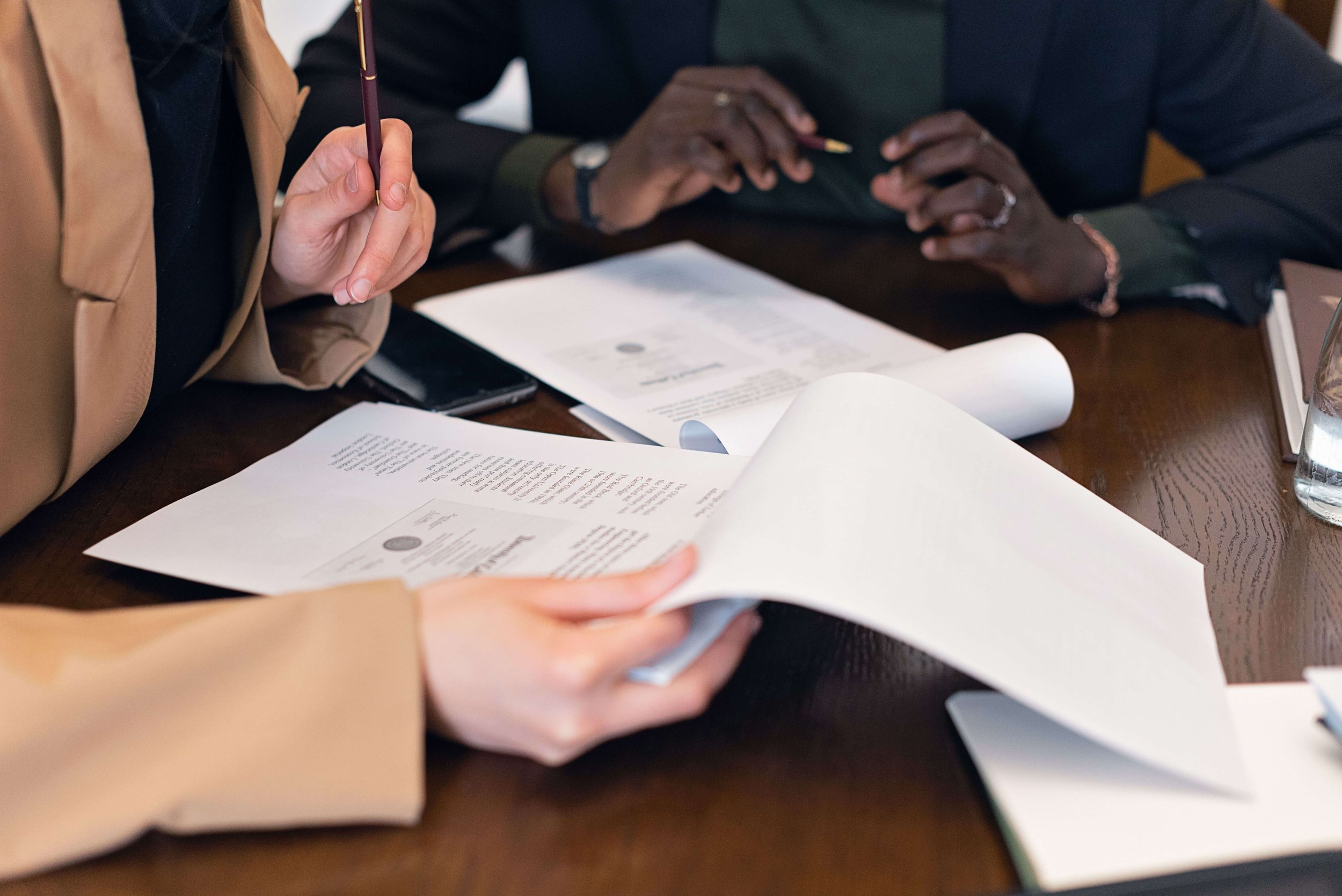 Three professionals seated around a table reviewing and handling multiple documents together. Thorough record review and open collaboration are the foundation of life care plans in Los Angeles, CA that hold up under the demands of complex litigation.