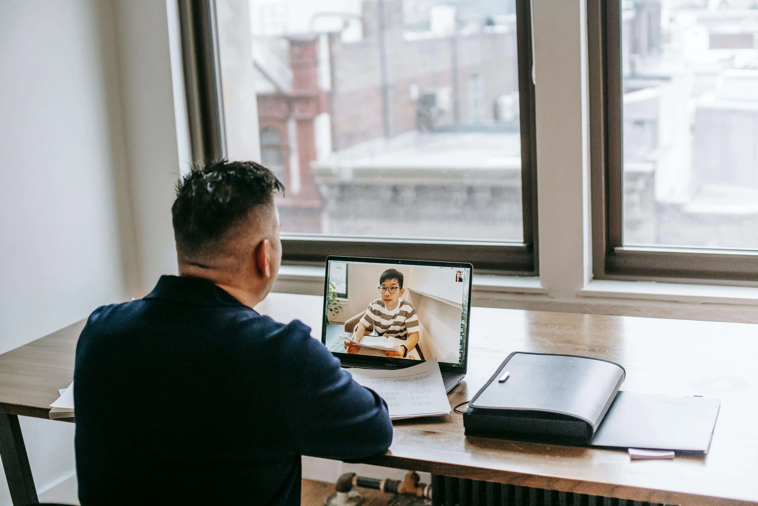Person in dark blazer participating in virtual meeting on laptop at wooden desk near window. Get the support you need after refusing a test through compassionate SAP evaluations in Las Vegas, NV.
