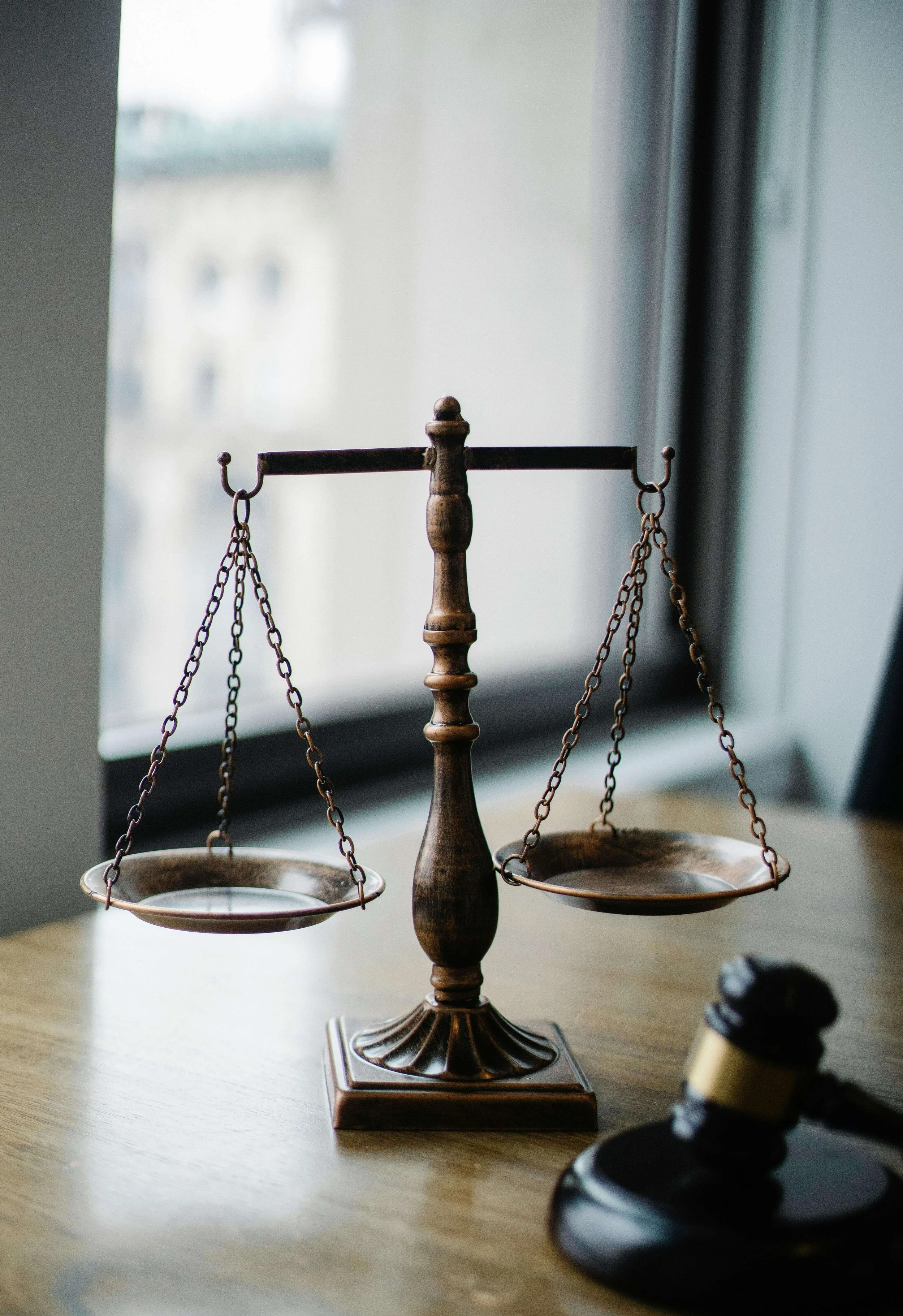 Brass scales of justice on wooden desk with gavel beside window. Legal evaluations in Las Vegas, NV provide objective, trauma-informed assessments that support clarity and fairness in immigration, family court, and civil matters.