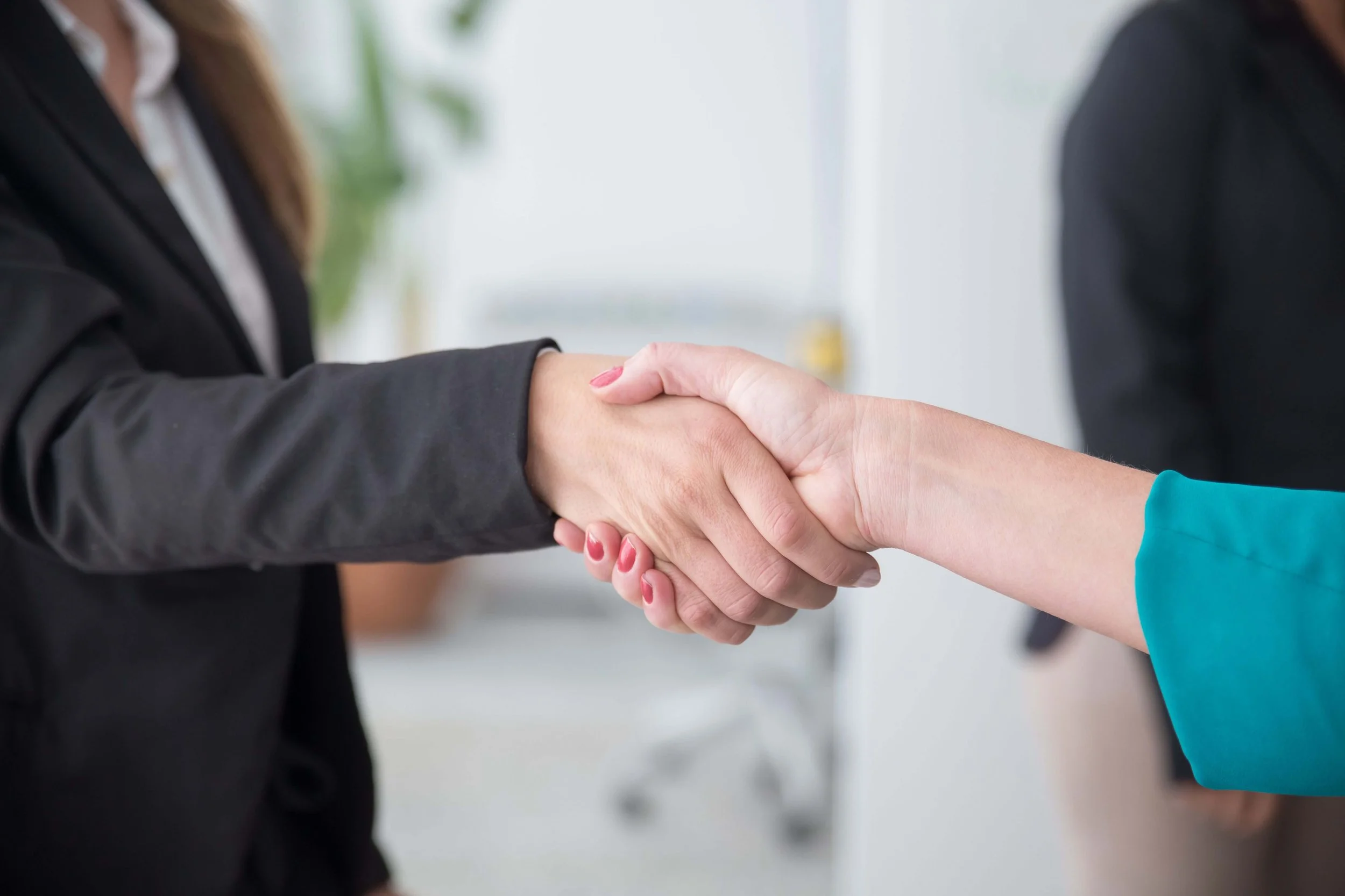 Two women shaking hands in a professional setting with one wearing a black blazer and the other a teal top. Working with the right clinical team ensures that life care plans in Los Angeles, CA are built on accurate facts not common misconceptions.