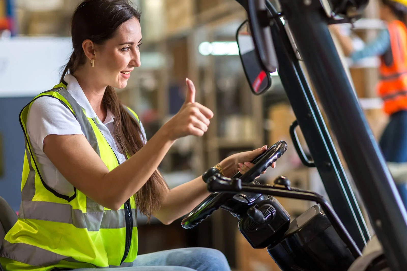 Female warehouse worker in safety vest giving thumbs up while operating forklift in industrial facility. Build healthier coping strategies for shift work with supportive SAP evaluations in Las Vegas, NV.