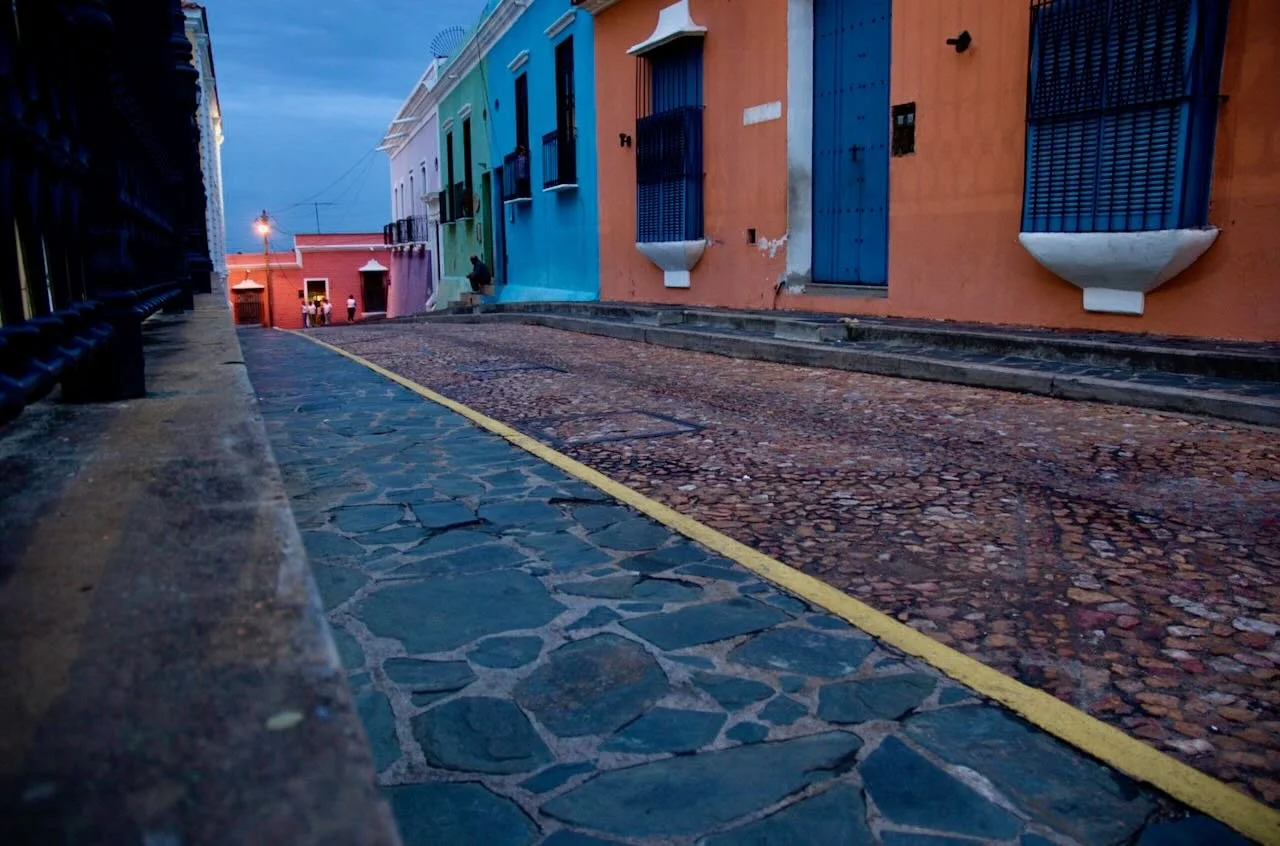 Colorful buildings along a cobblestone street, with a yellow-painted curb, during dusk.