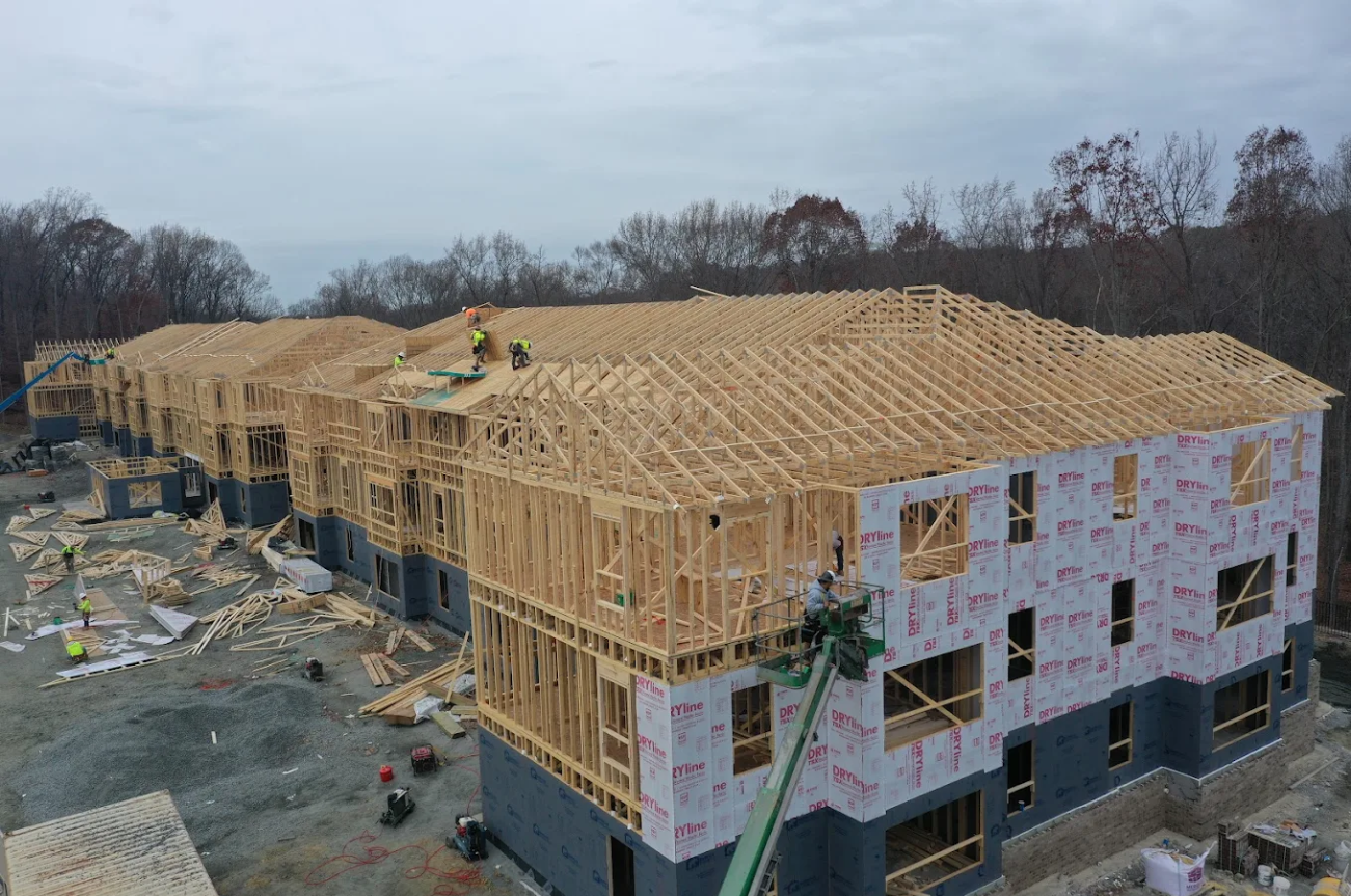 Construction site with wooden framing of a multi-story building in progress, workers on site, and a crane lifting materials.