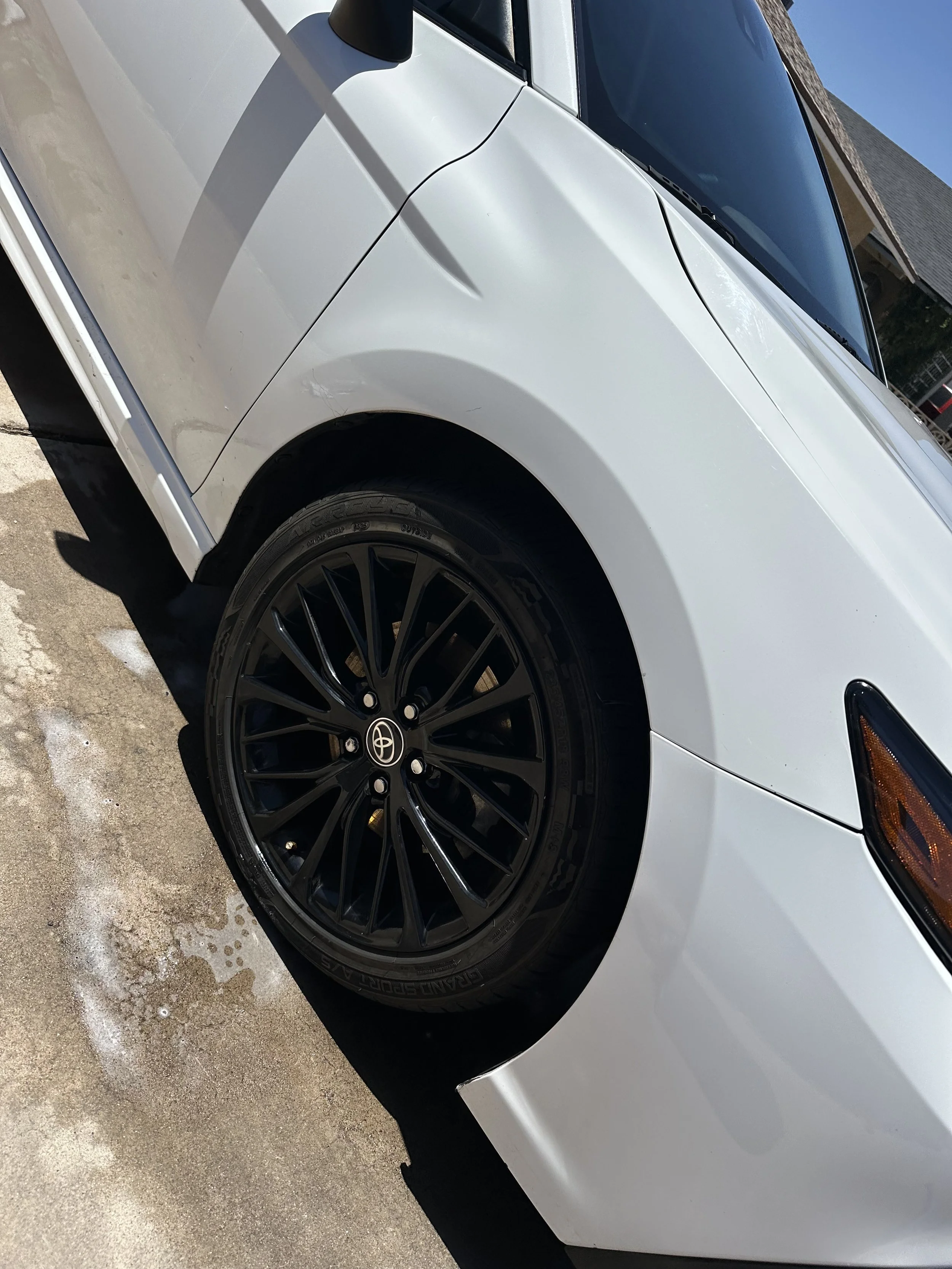Close-up of a white Toyota car with black alloy wheels parked on a dirt surface.