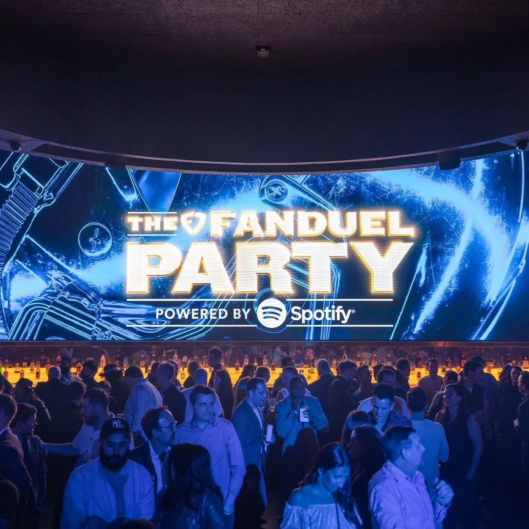 Crowd of people attending The Fanduel Party, powered by Spotify, with a large digital screen displaying event branding and musical graphics.