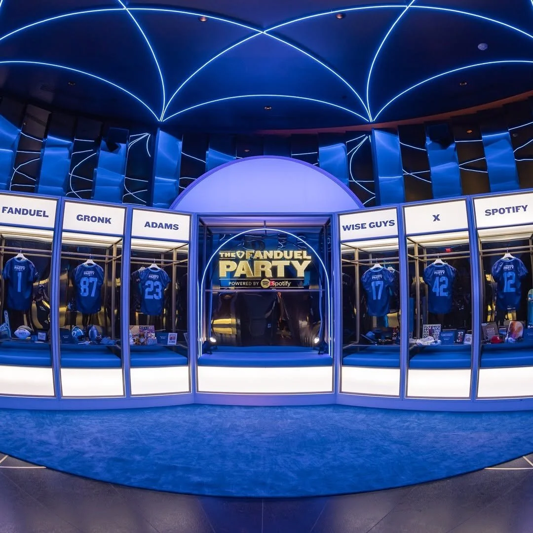 An indoor display for a fantasy football league called 'The Fanduel Party', featuring jerseys with player names and numbers, and signage indicating sponsors like Spotify. The display has a futuristic, blue-lit design with neon accents.