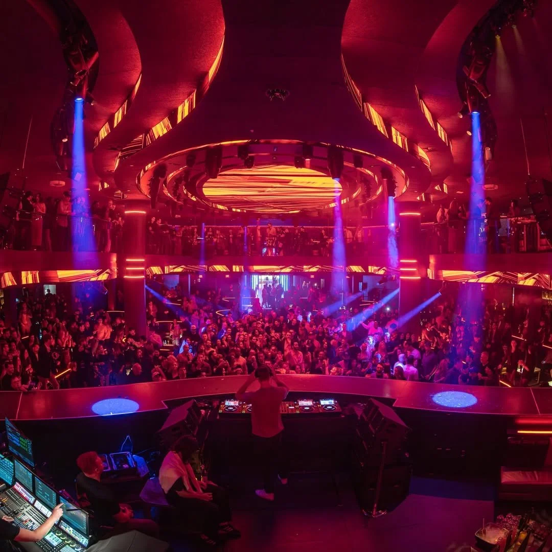 Crowd inside a nightclub with colorful lighting and a DJ booth in the foreground.