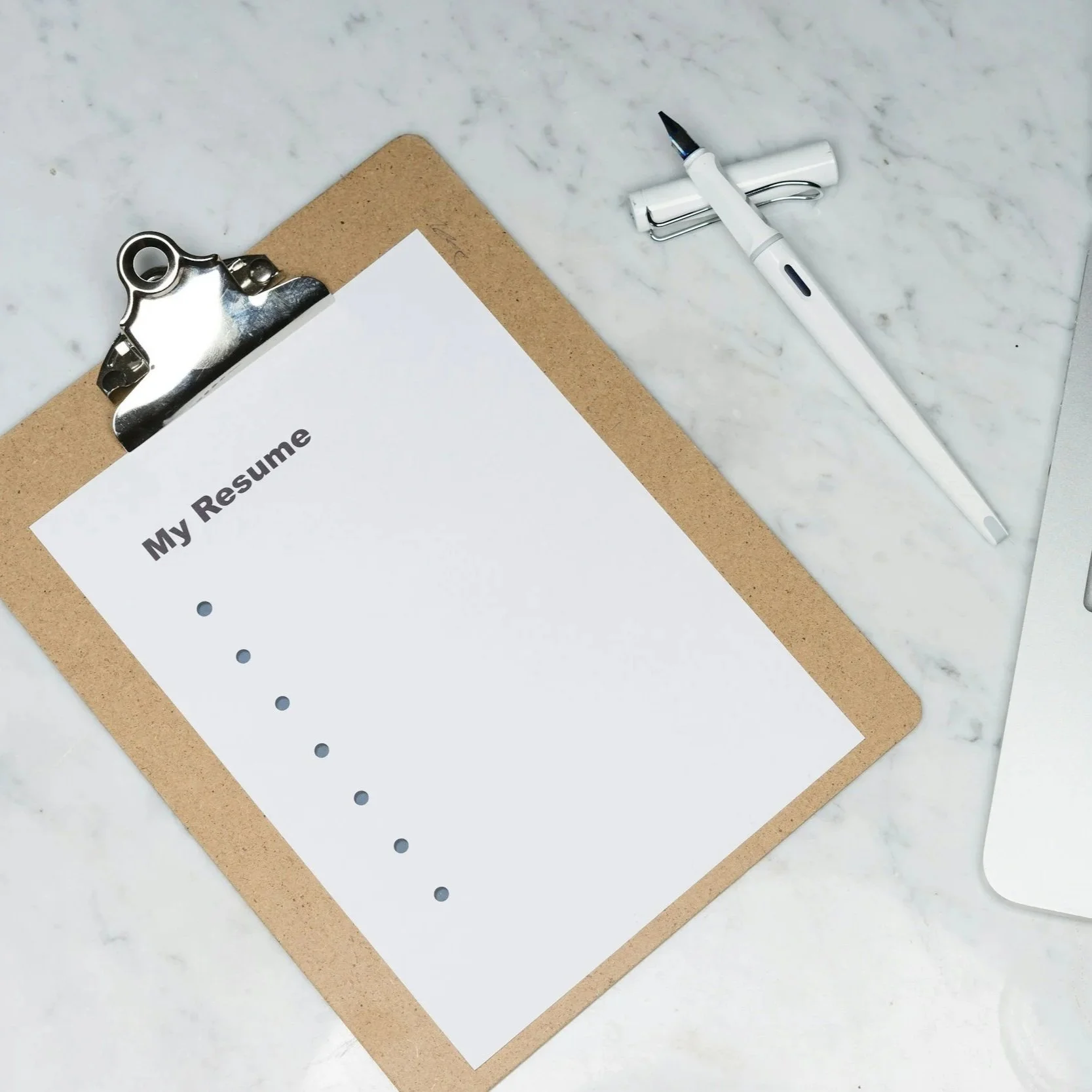 A clipboard with a resume template titled 'My Resume' on a marble desk, with a white pen and a silver paperclip nearby.