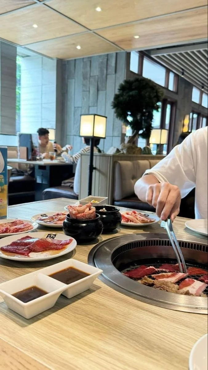 Personas cocinando carne en un restaurante de parrillada con mesas llenas de carne y salsas