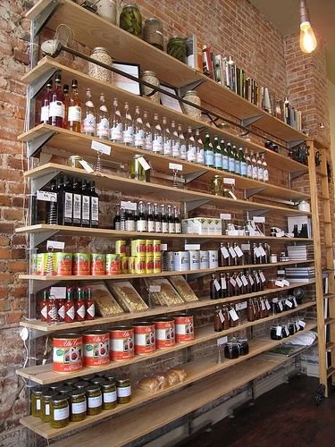 Estantería de madera con frascos, botellas y productos en una tienda, con paredes de ladrillo visible.