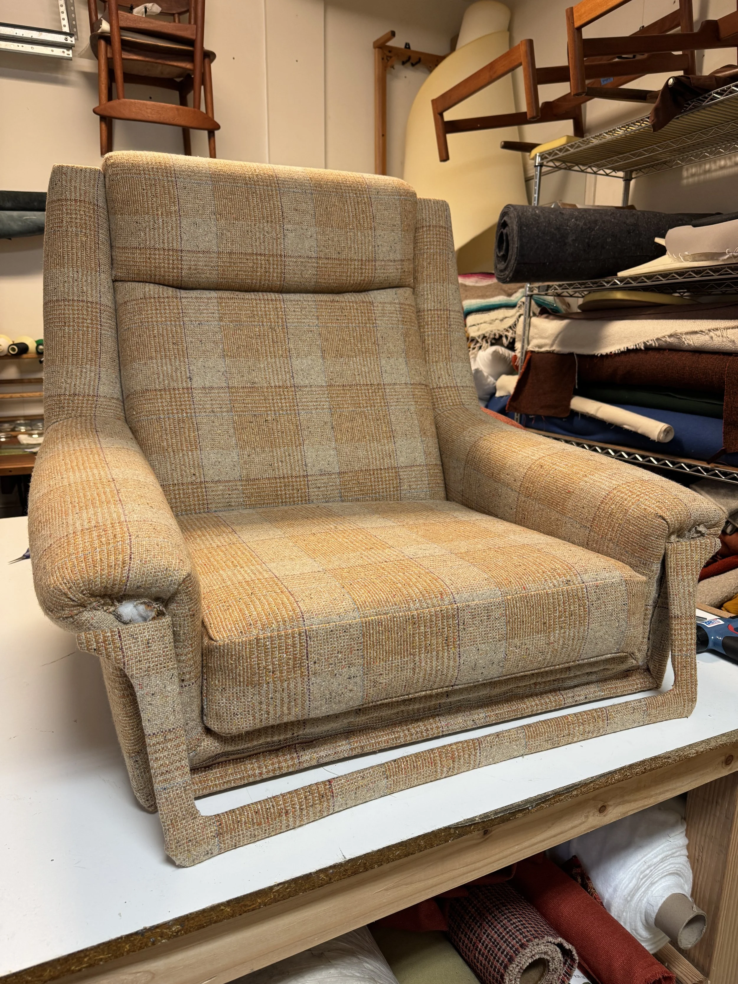 High-back Danish modern lounge chair being upholstered in Luum Mélange Check wool, showing the plaid alignment across the backrest, arms, and seat.