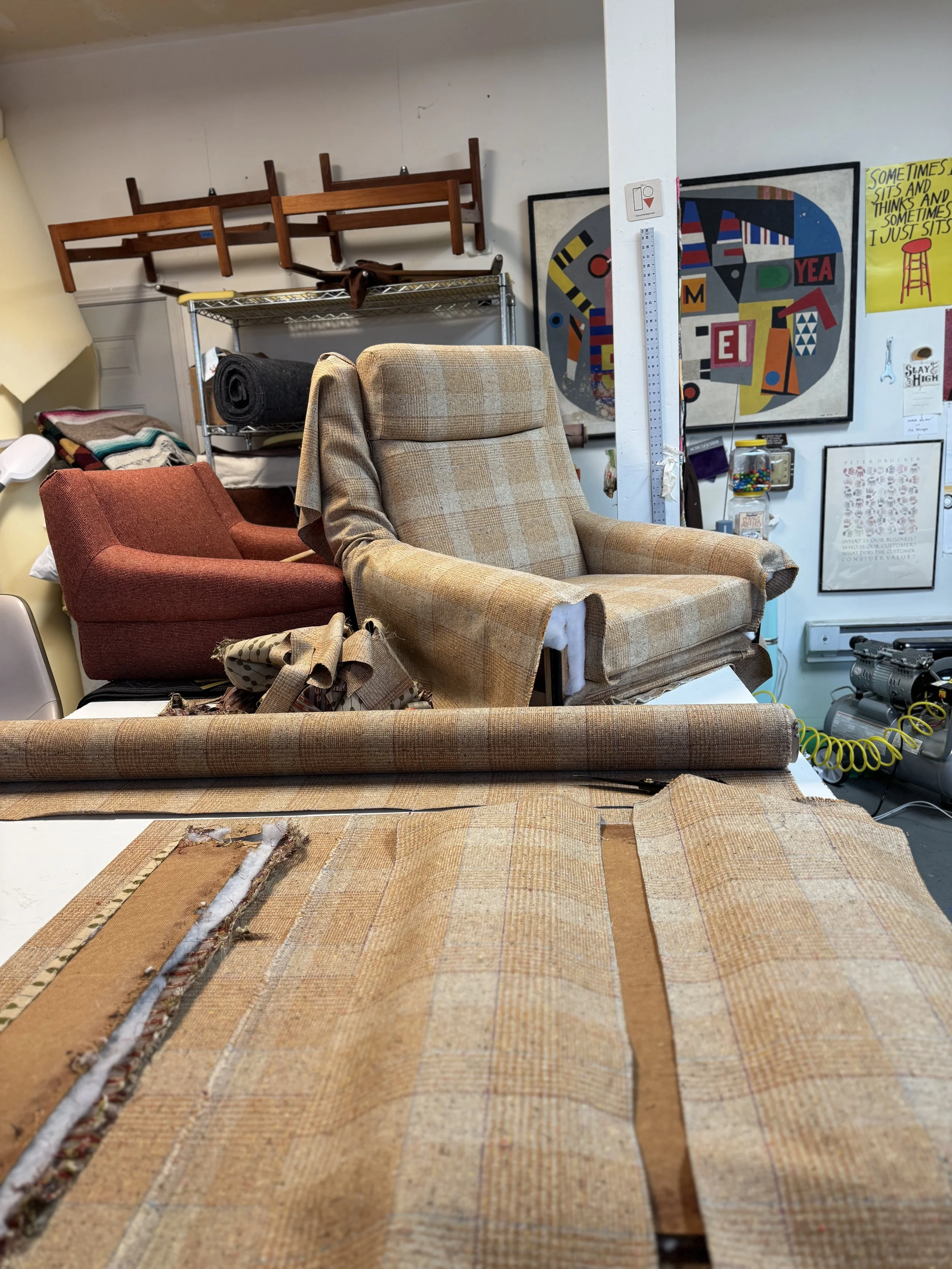 Danish modern lounge chair undergoing reupholstery in the Rescue Vintage workshop, with plaid fabric pieces arranged on the worktable.