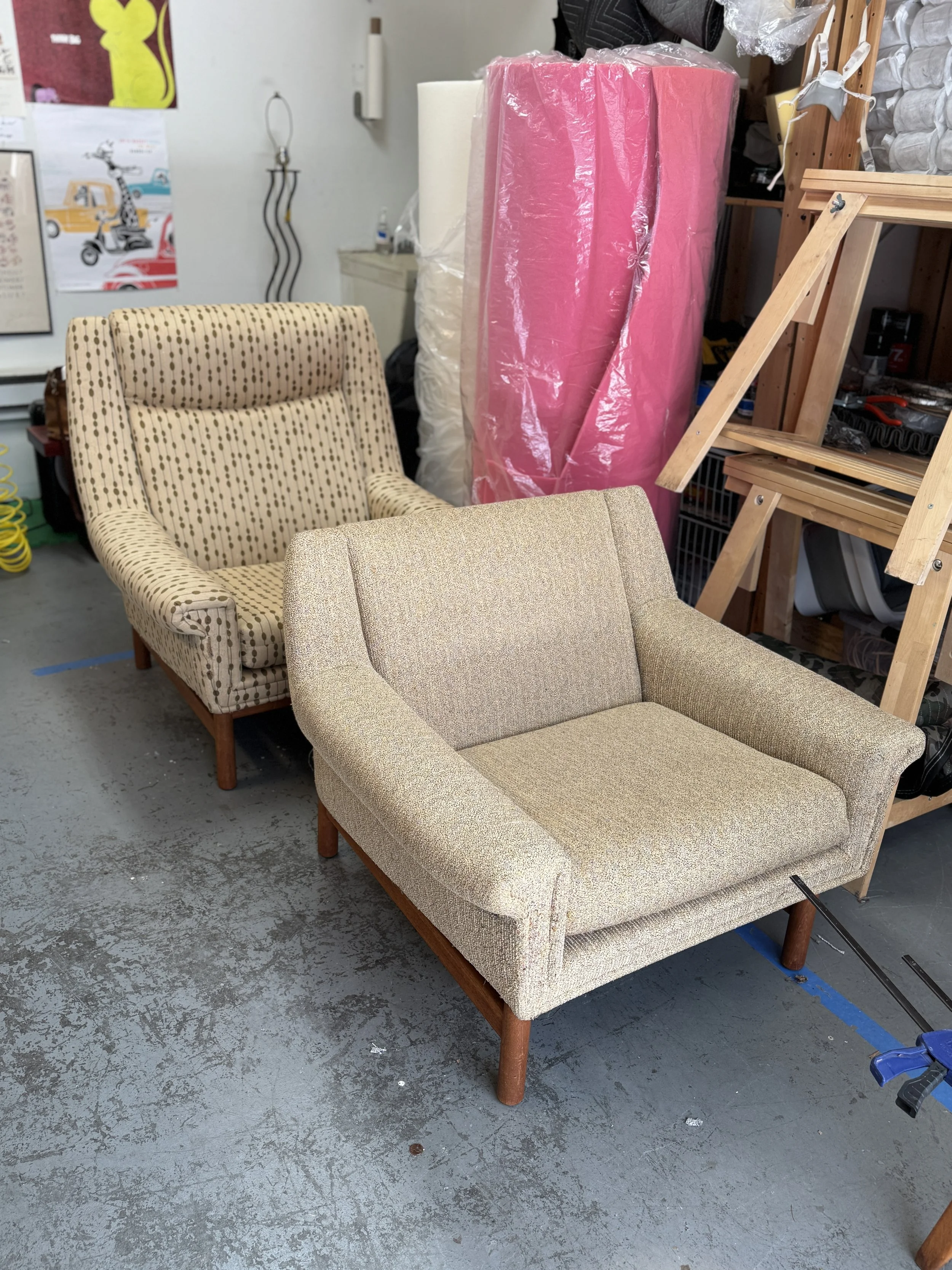 Pair of vintage Danish modern lounge chairs with their original light-colored upholstery, photographed in the workshop before restoration.