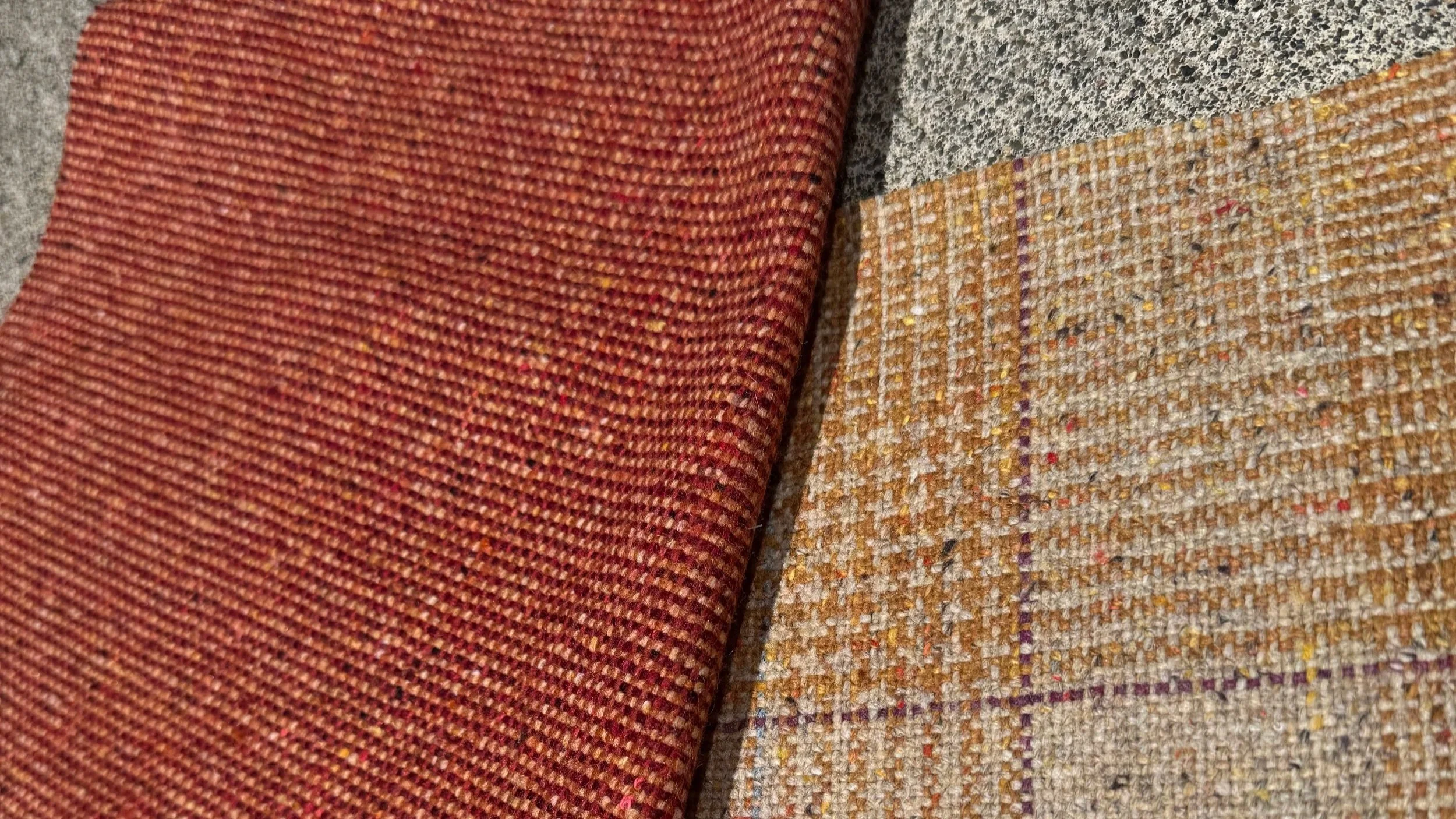 Close-up of Luum Wool Fleck in 'Corten' - a rust red, and Melange Check in 'Goldspeck' wool upholstery fabric in ochre and cream with purple plaid stripes, selected for a Danish modern living room set.