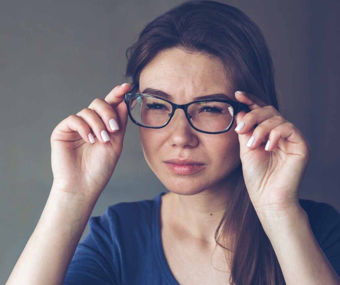 A woman adjusting her glasses and squinting, wearing a dark blue top.
