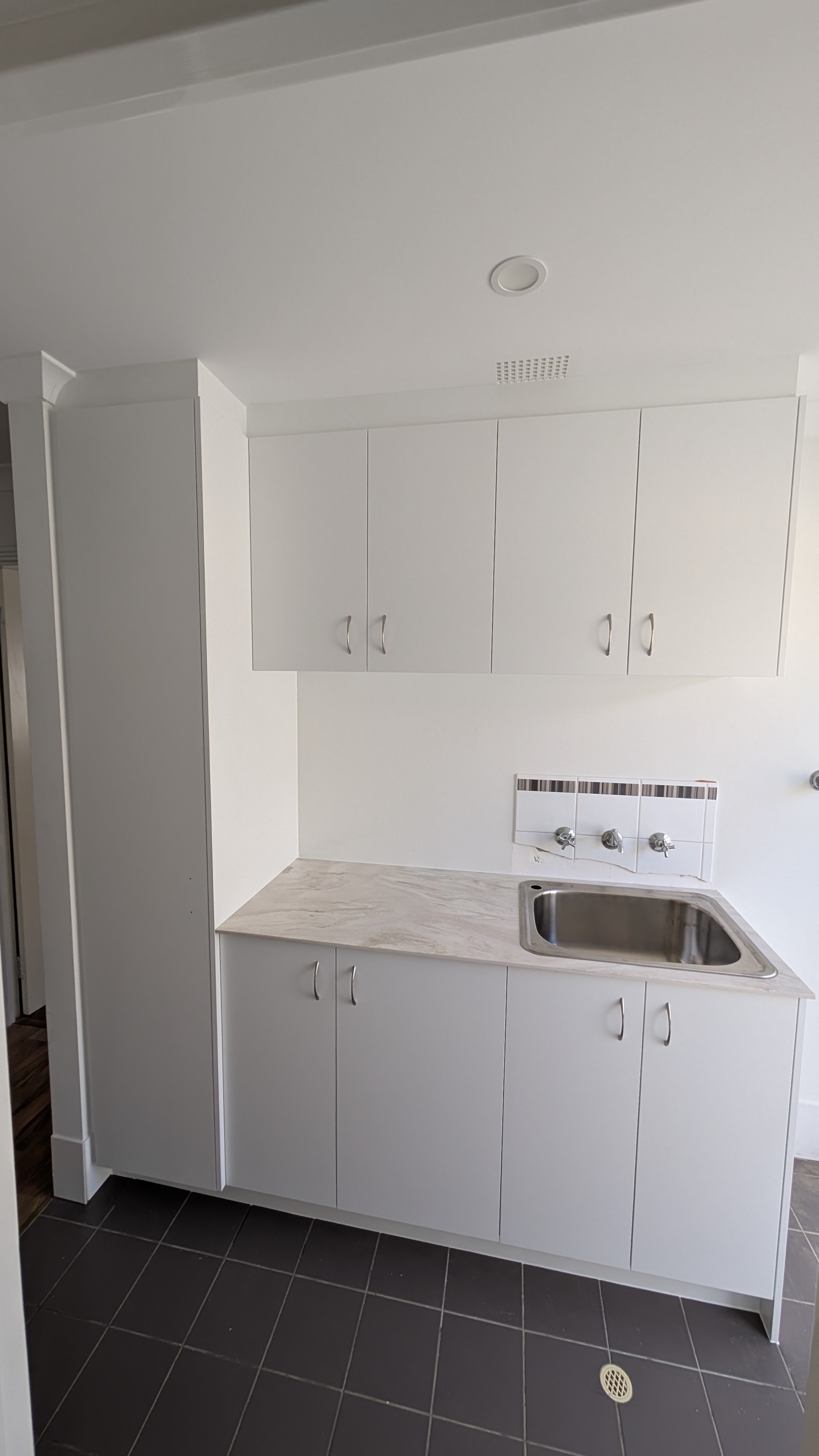 Small white kitchen with upper and lower cabinets, a marble countertop, stainless steel sink, and a tiled backsplash with black accent tiles.