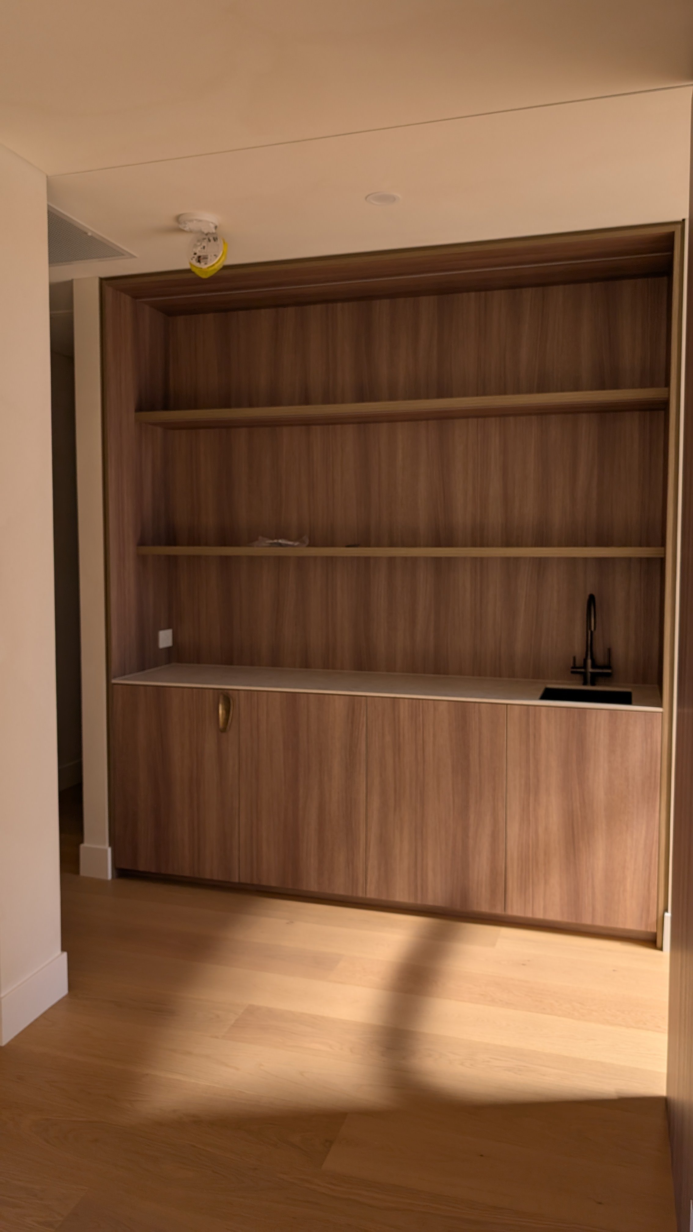 Wooden built-in wall unit with shelves, a countertop, and a black sink with a tall black faucet.