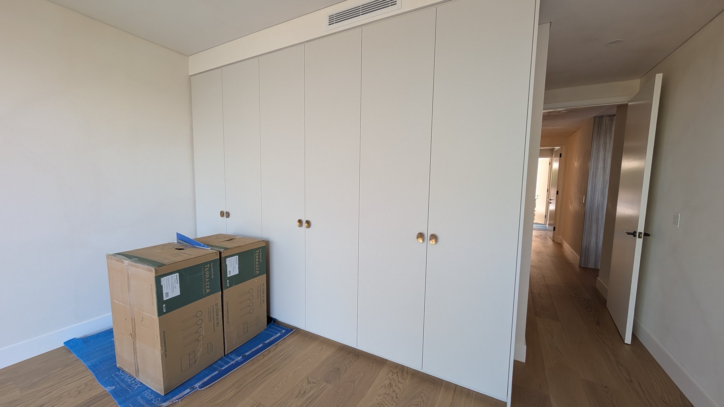 Empty room with white built-in closet doors and two cardboard boxes on a blue moving pad on hardwood floor.