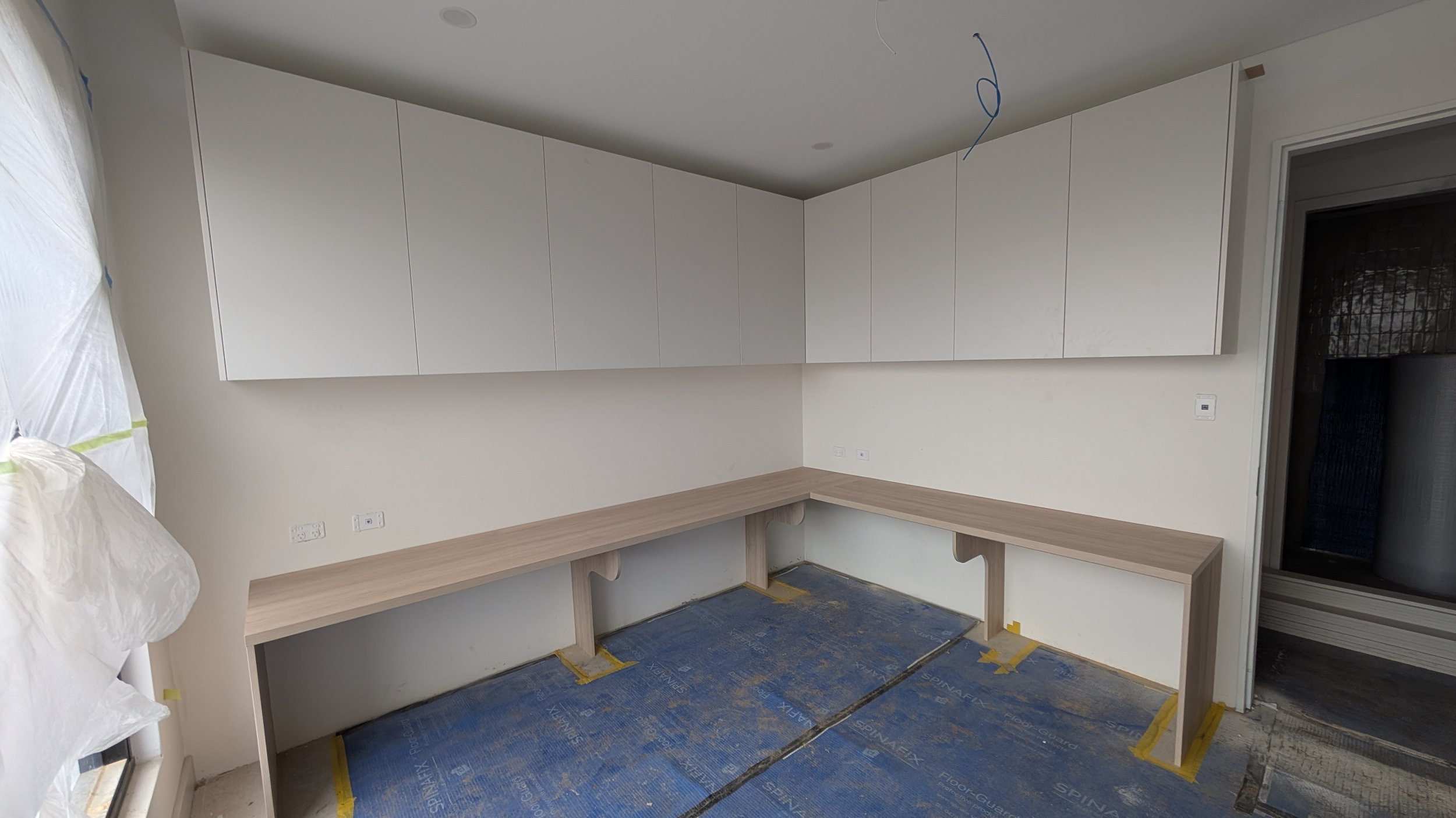 Room under construction with white cabinets, a long wooden counter, blue protective floor covering, and construction materials.