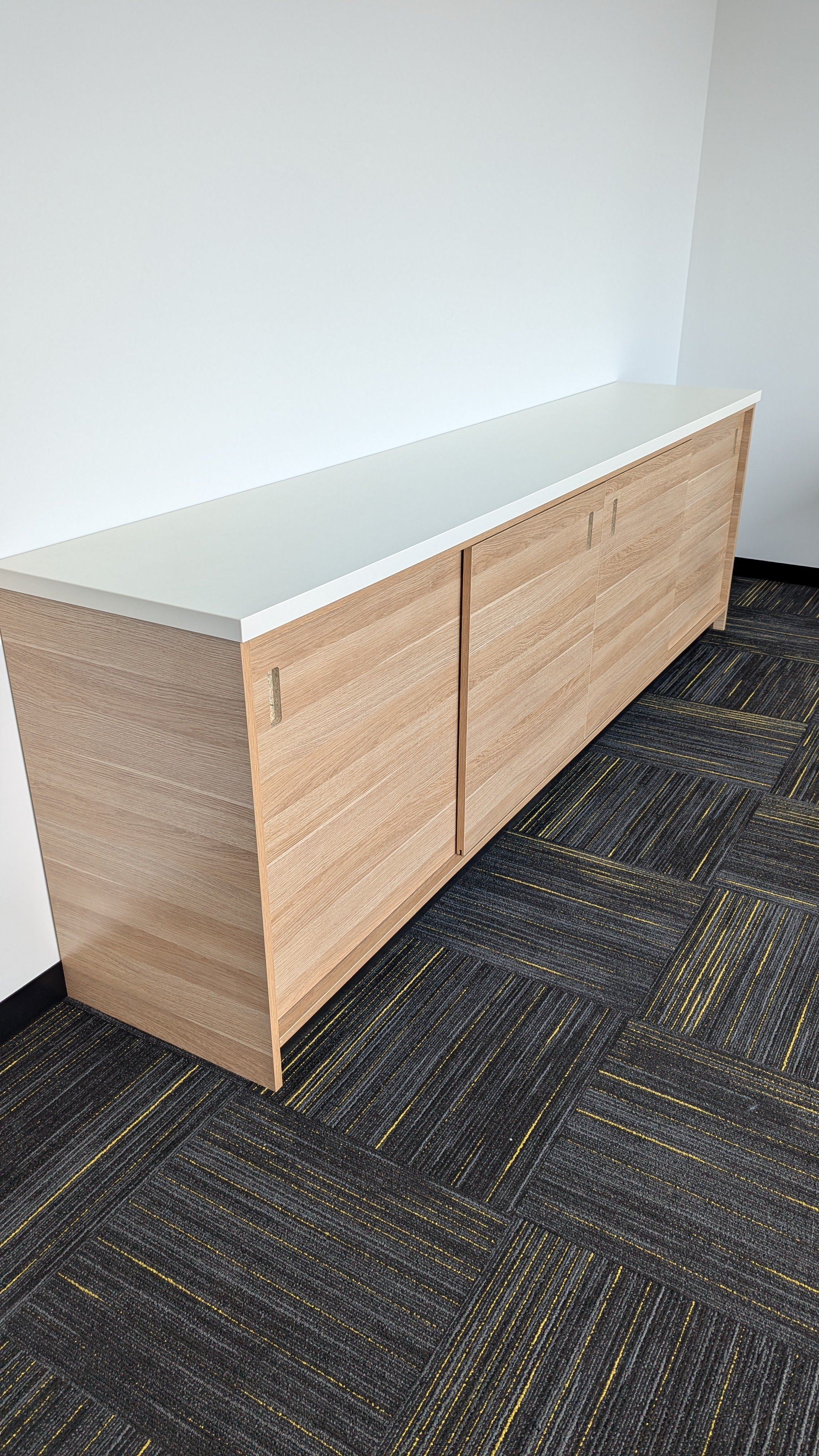 Wooden cabinet with sliding doors on a patterned carpeted floor against a white wall.