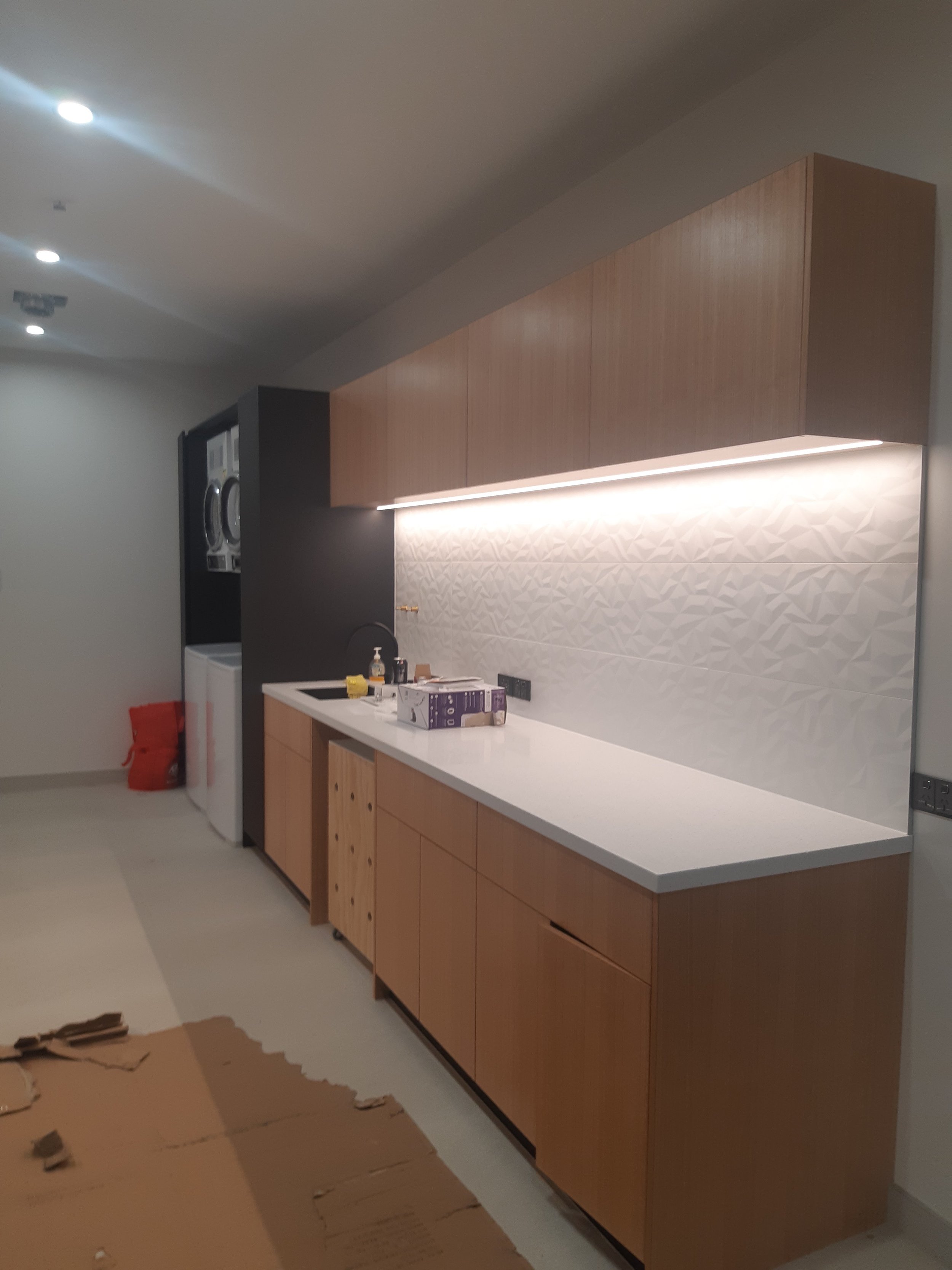 Modern kitchen with wooden cabinets, white textured backsplash, and under-cabinet lighting.