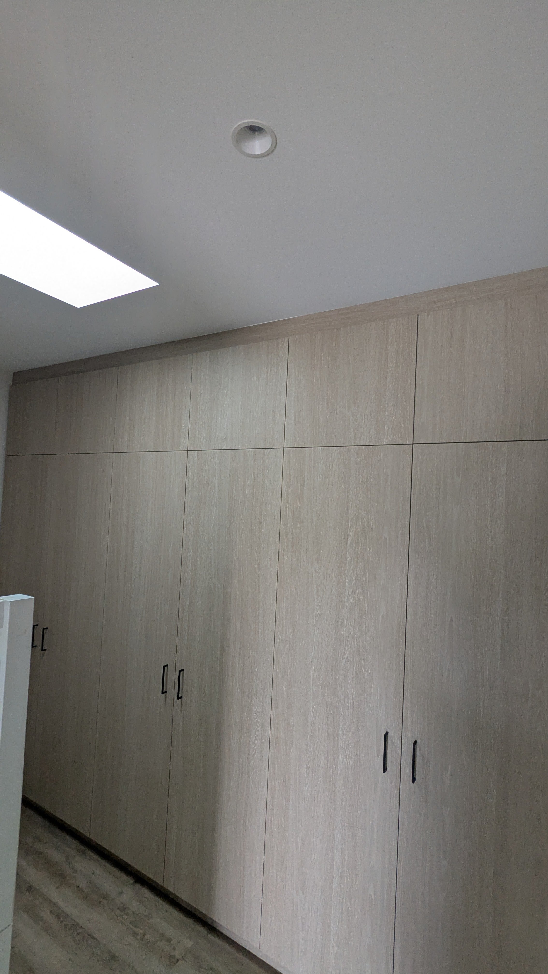 Off-white built-in cabinets with black handles in a room with a white ceiling, a recessed light, and a ceiling vent.