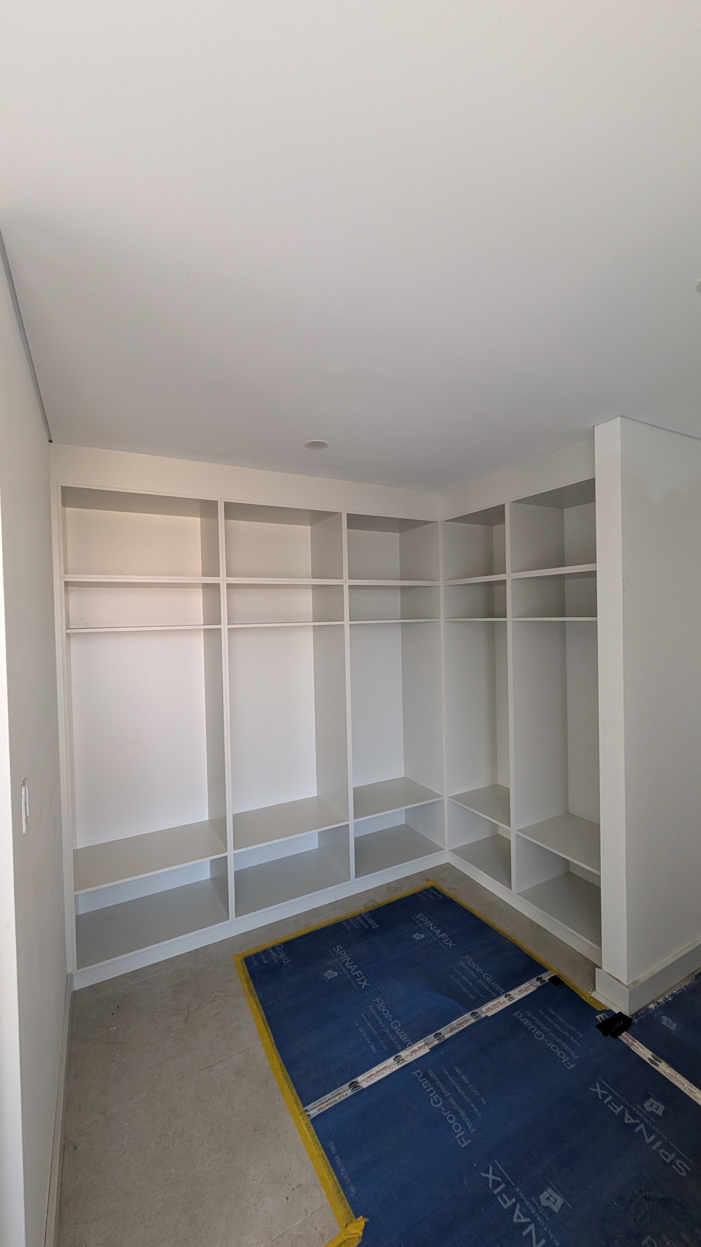 Empty built-in white closet with multiple shelves and compartments, with blue protective floor covering in front.