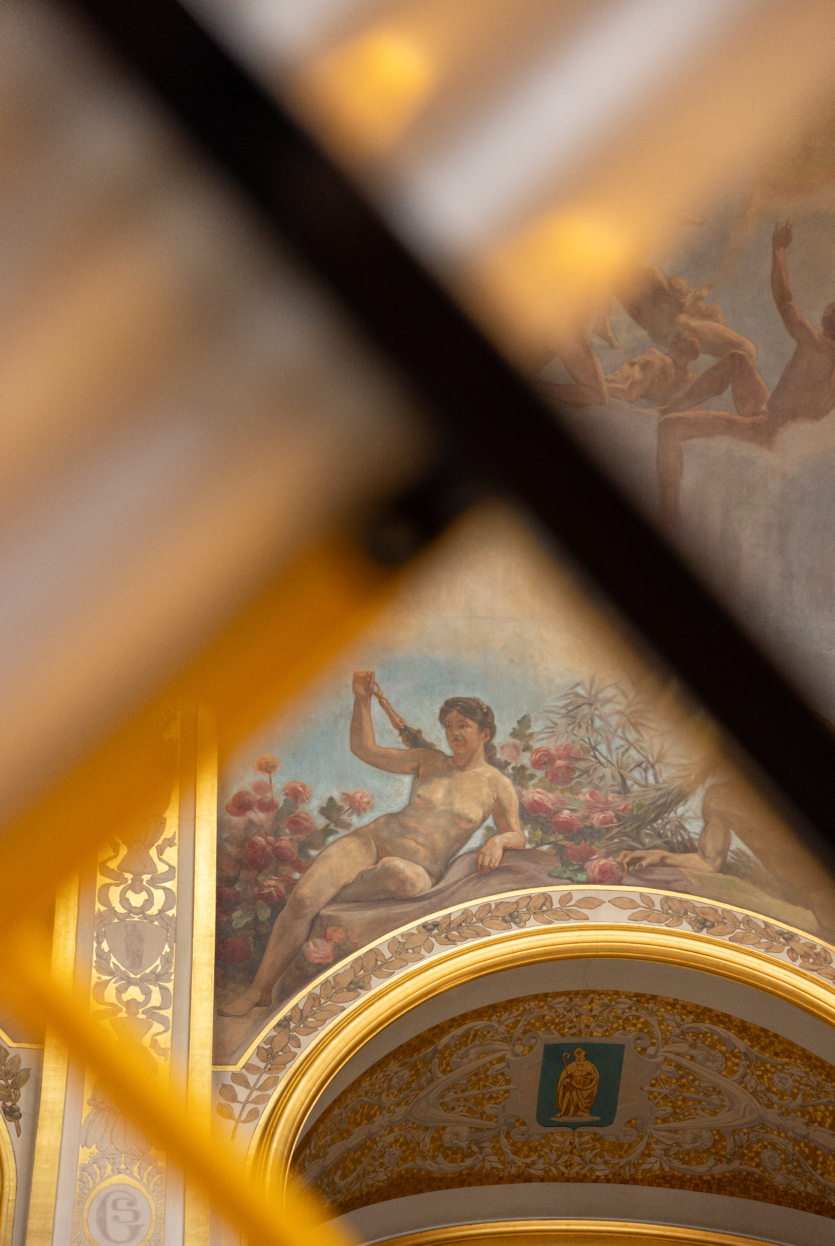 A classical mural painting of a reclining nude woman surrounded by flowers, located on an ornate, arched ceiling inside a decorated building. La Maison communale de Saint-Gilles ceiling. 