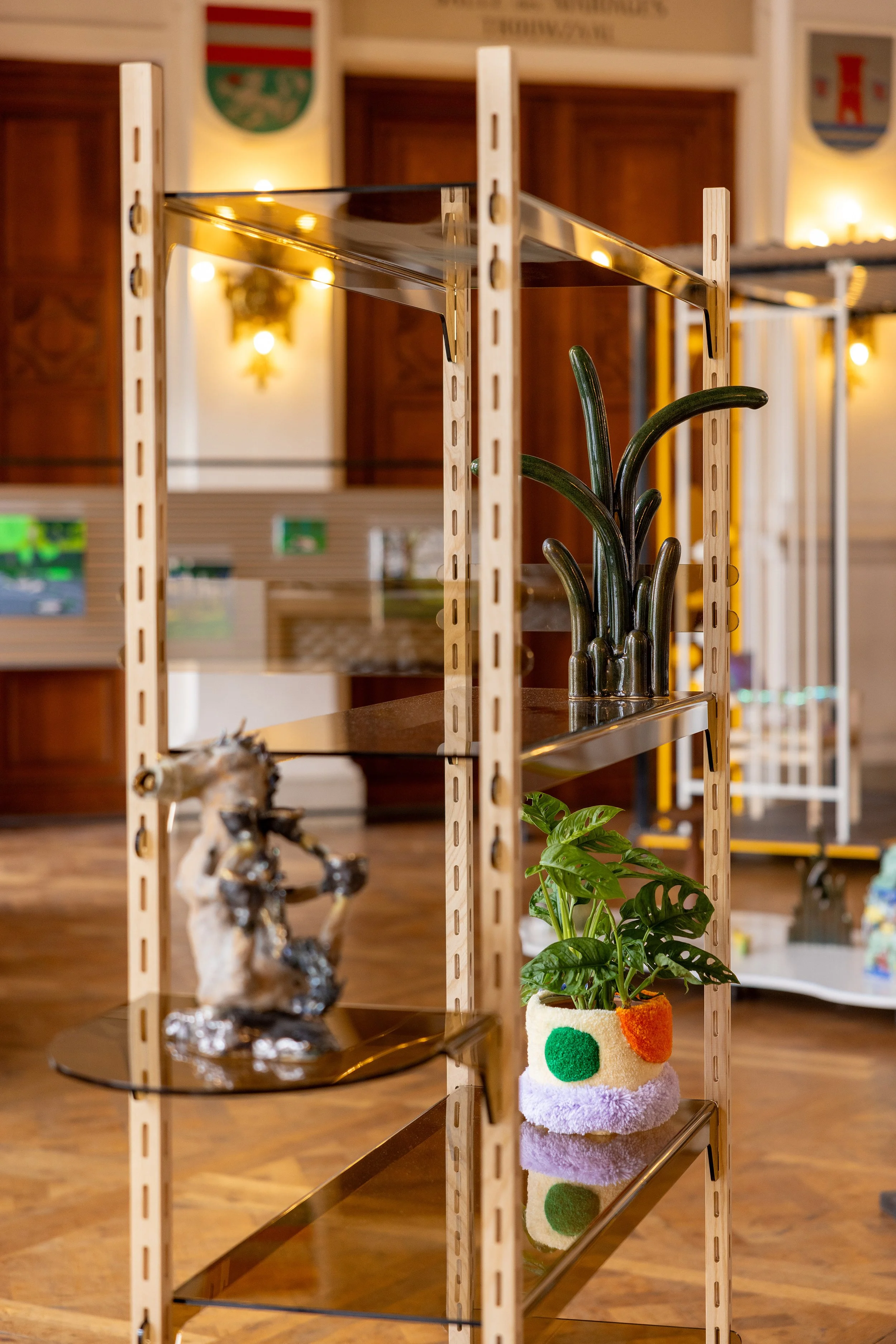 Display shelf in exhibition with various decorative objects including a ceramic horse sculpture, a glass sculpture, and a tufted plant cover.