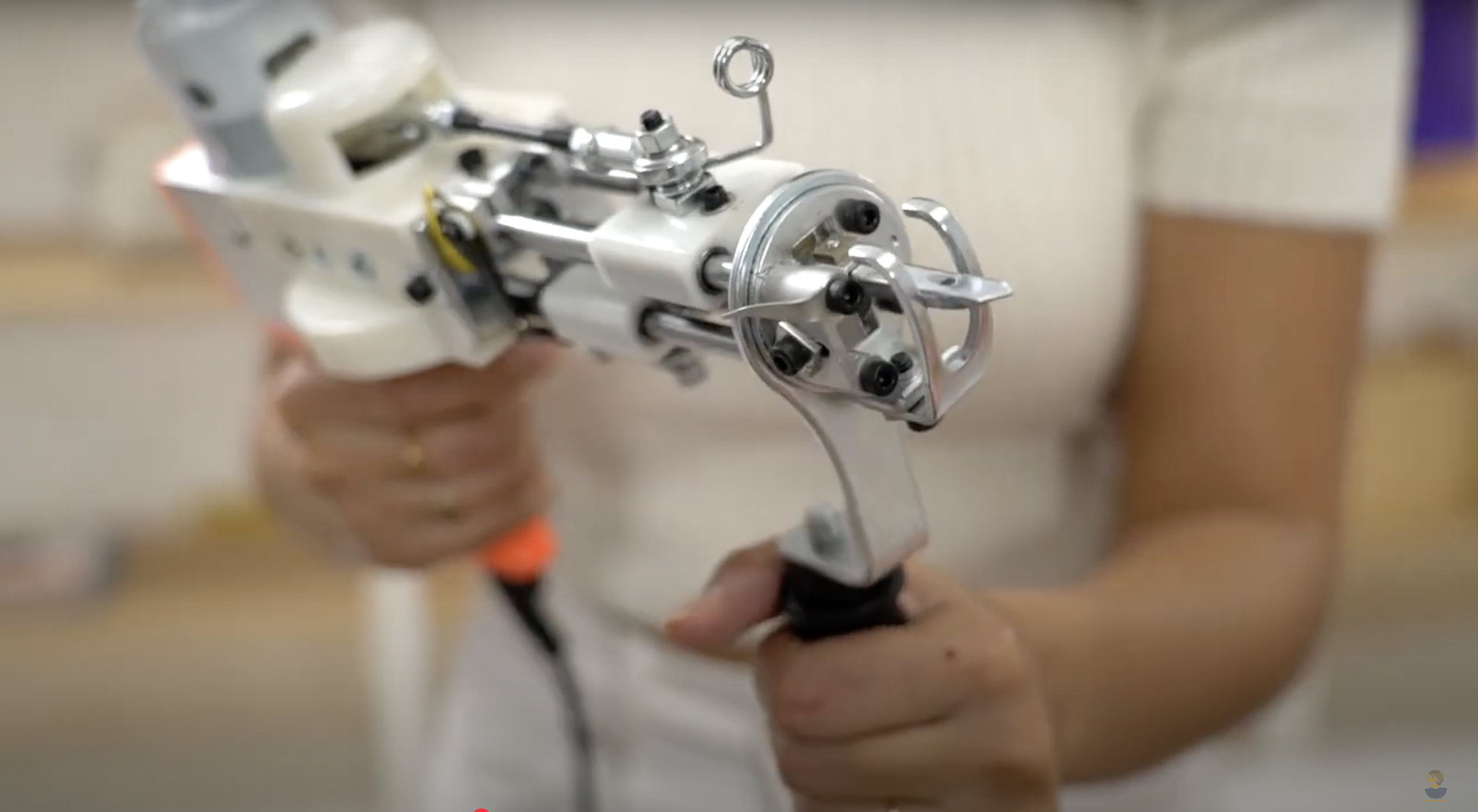 Person holding a small, silver, mechanical device with black screws and metallic parts called a tufting gun.