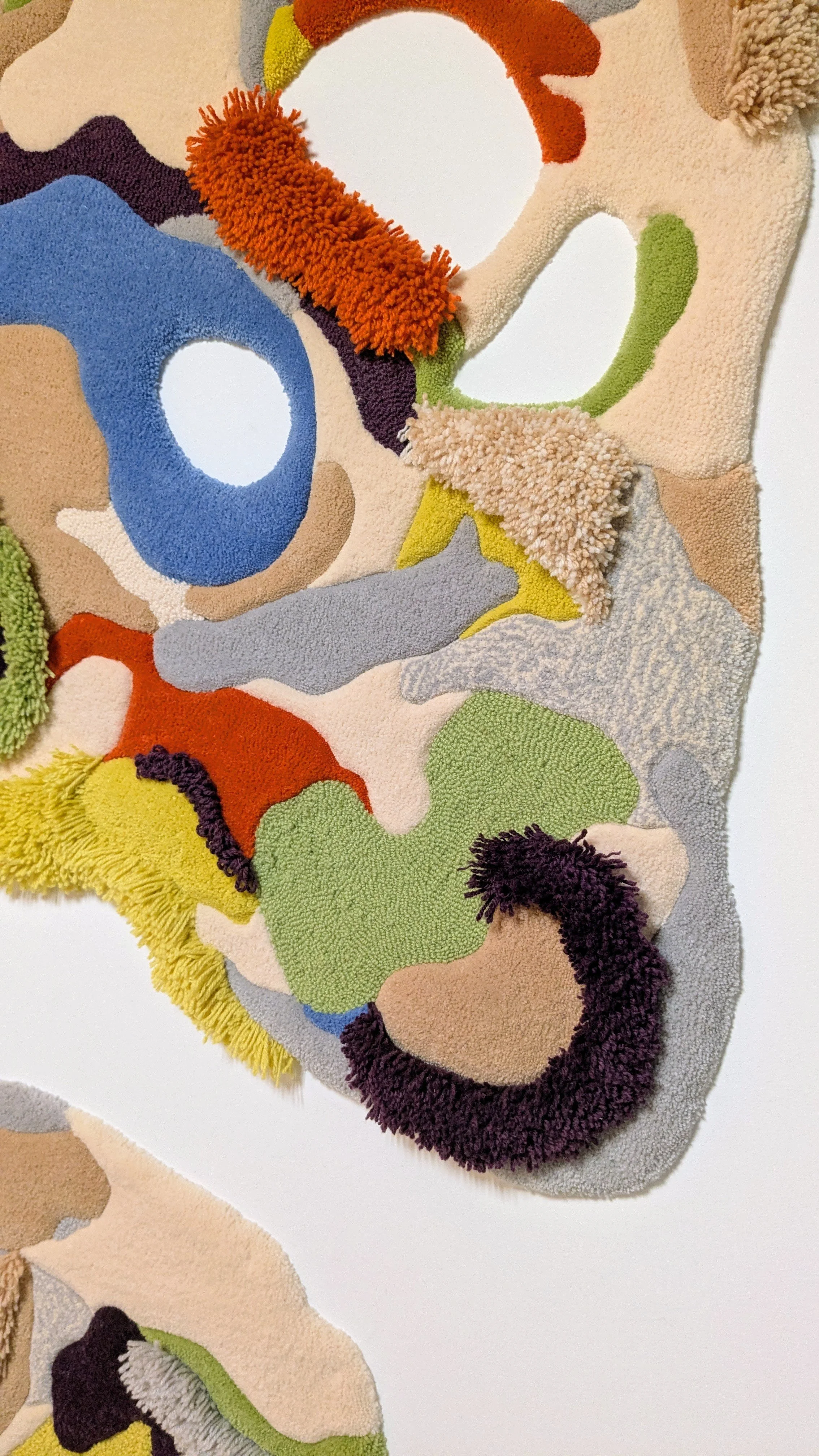 Colorful abstract tufted textile art with various textured and pile heights fabric pieces in bright colors like orange, blue, green, yellow, purple, black, and beige.