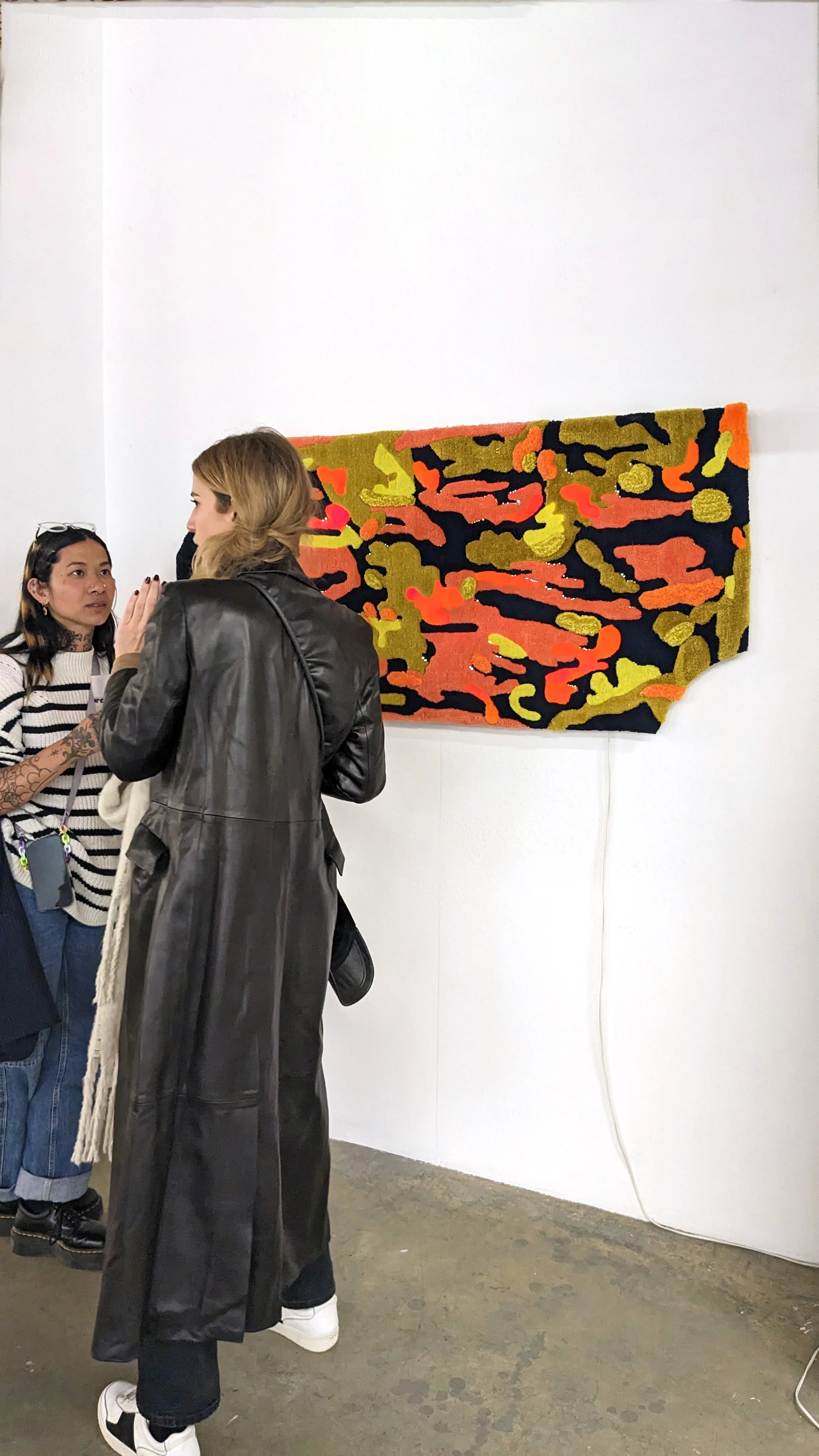 People talking in an art gallery with a colorful abstract tufted light box on the wall.