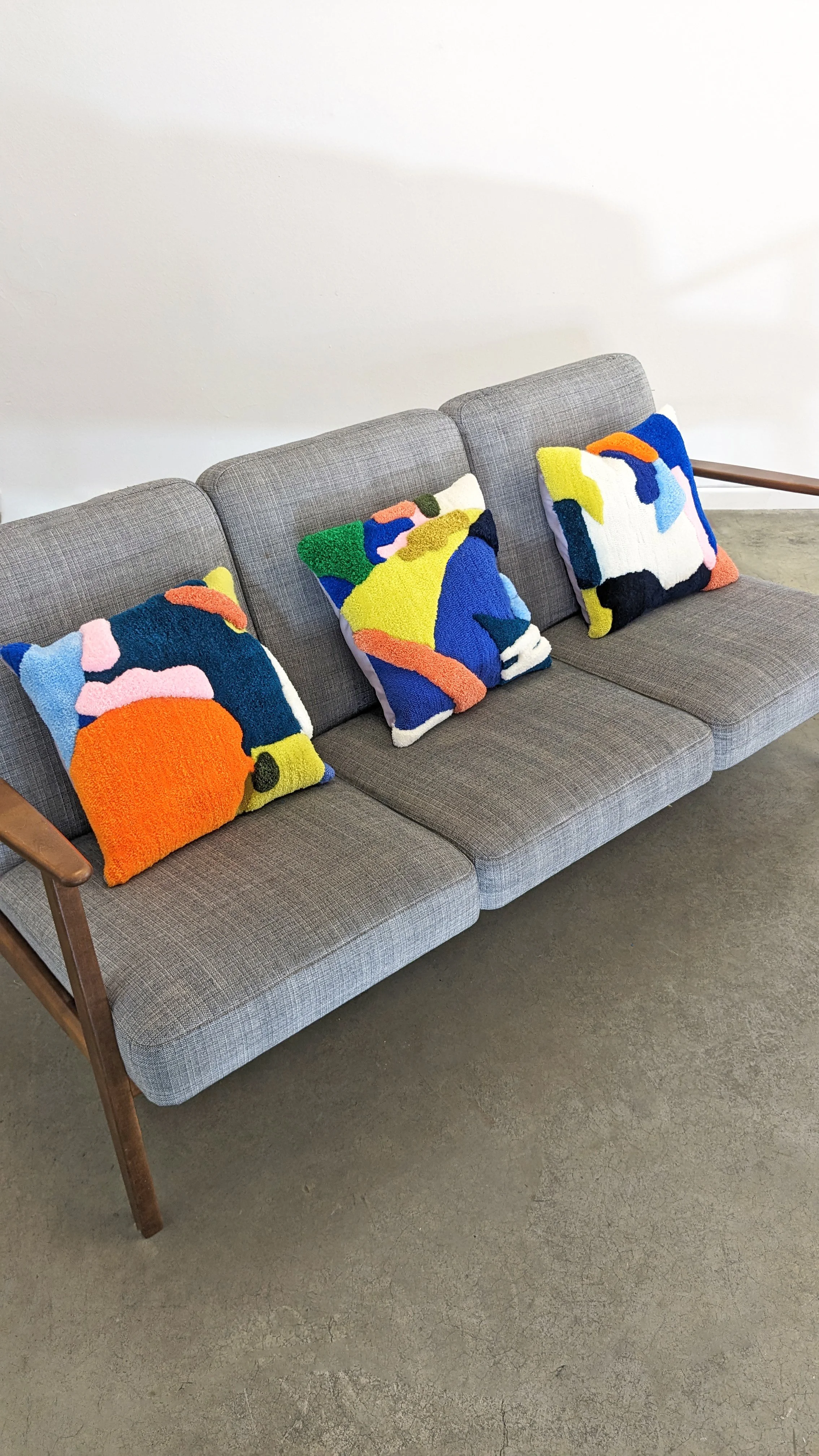 A gray upholstered sofa with wooden armrests, decorated with colorful abstract tufted throw pillows.