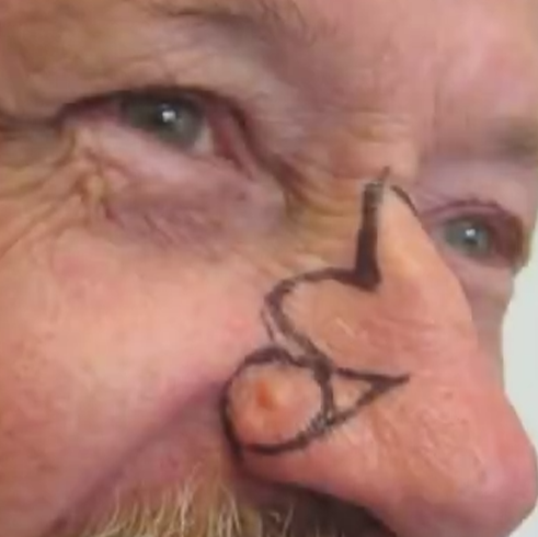 Close-up of a person's face with a nose painted to resemble a heart, with exaggerated facial wrinkles.