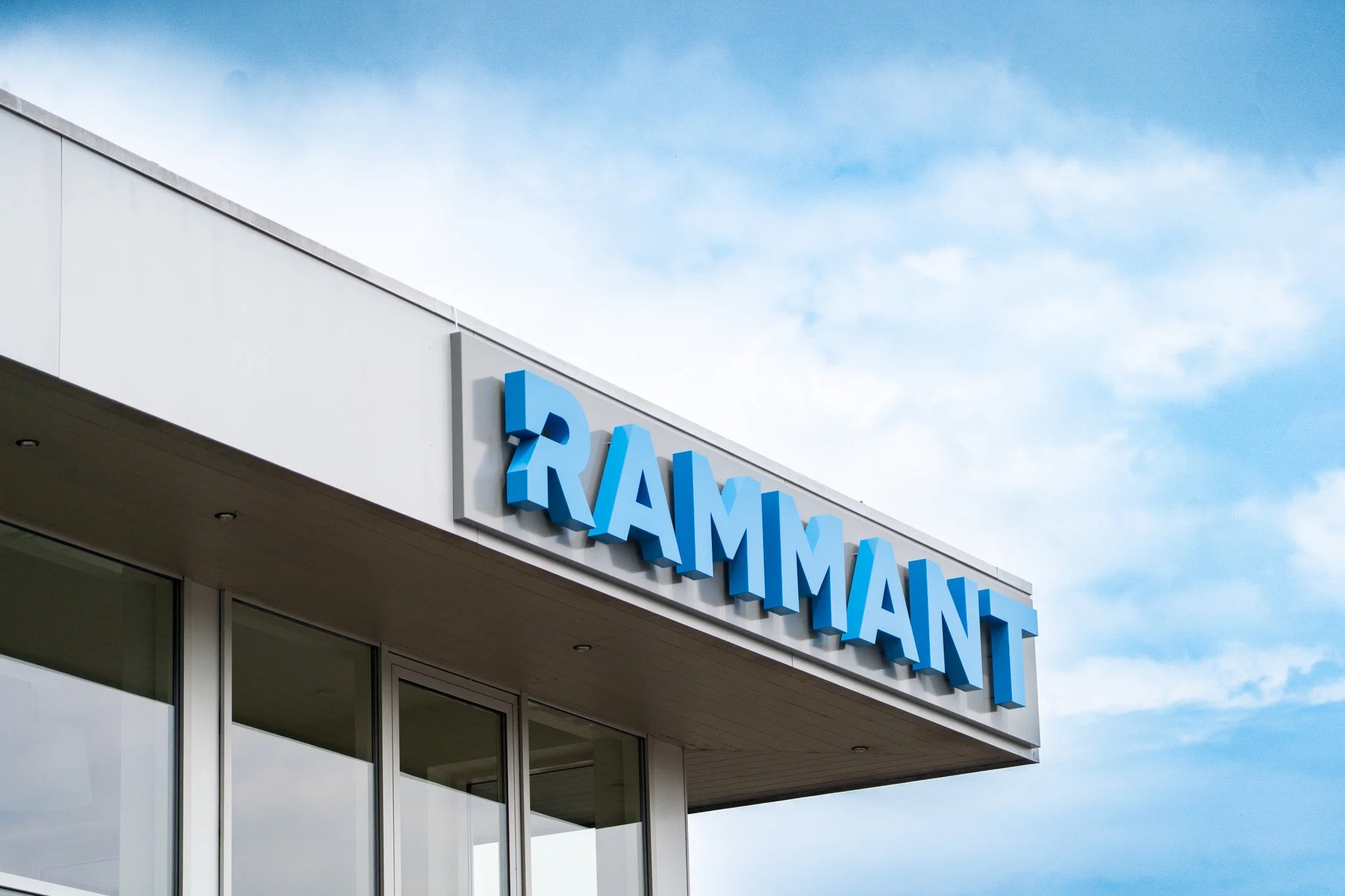 Veelzijdige ramenwinkel met blauwe verlichte letters op de gevel, uitzicht op een heldere blauwe lucht met enkele wolken.