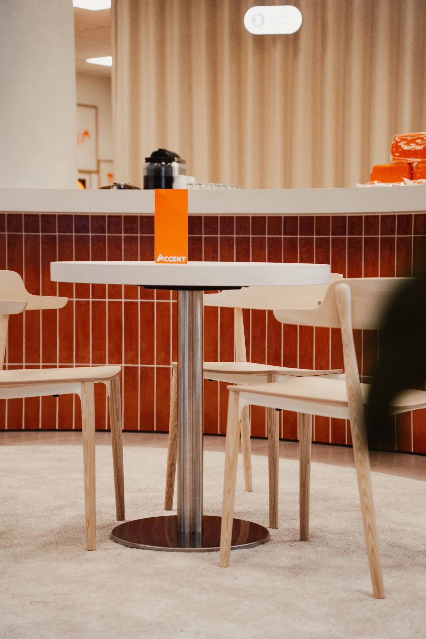 Een leeg tafeltje met drie houten stoelen in een restaurant of cafésetting, met een rode en beige achtergrond.