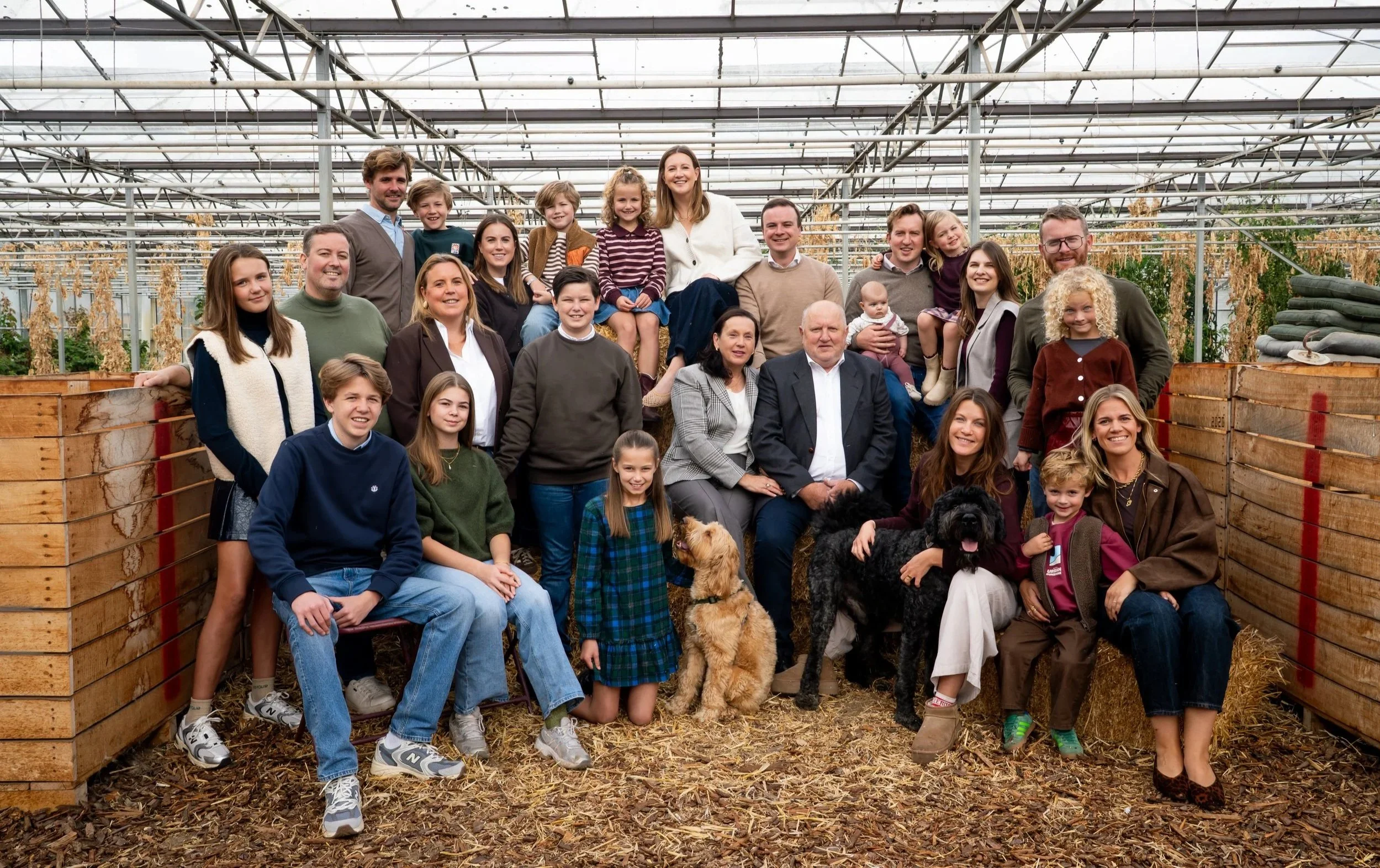 Een grote groep mensen, inclusief kinderen en honden, poseren in een botanische tuin of kas.