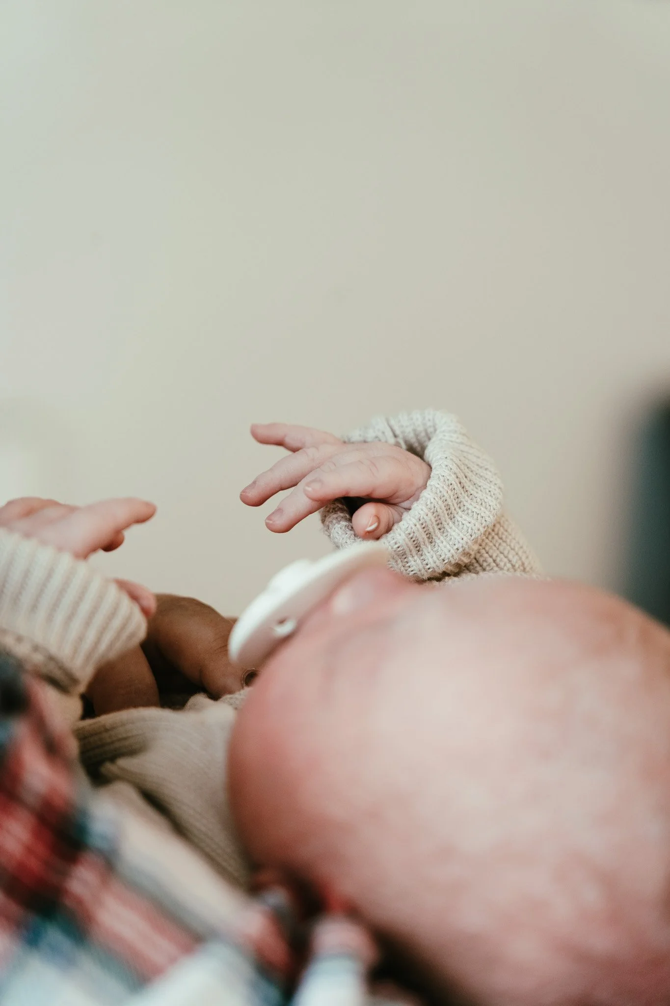 Close-up van een pasgeboren baby met een pacifier in de mond, vastgehouden door een volwassene, met alleen handen en een schouder zichtbaar.